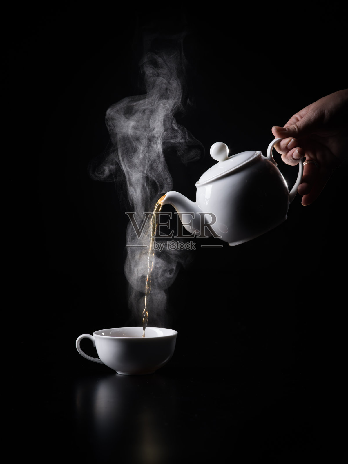 将热茶倒入黑色背景的杯子中。照片摄影图片