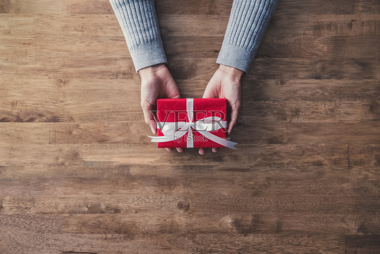 女人手在灰色毛衣在木头桌子送红色圣诞礼品盒照片摄影图片