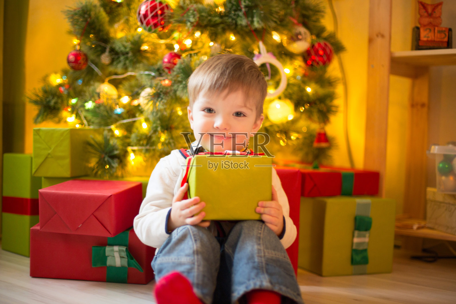 快乐的小男孩拿着圣诞礼物在圣诞夜装饰的房间里。晴朗的早晨或白天。圣诞节或新年假期照片摄影图片