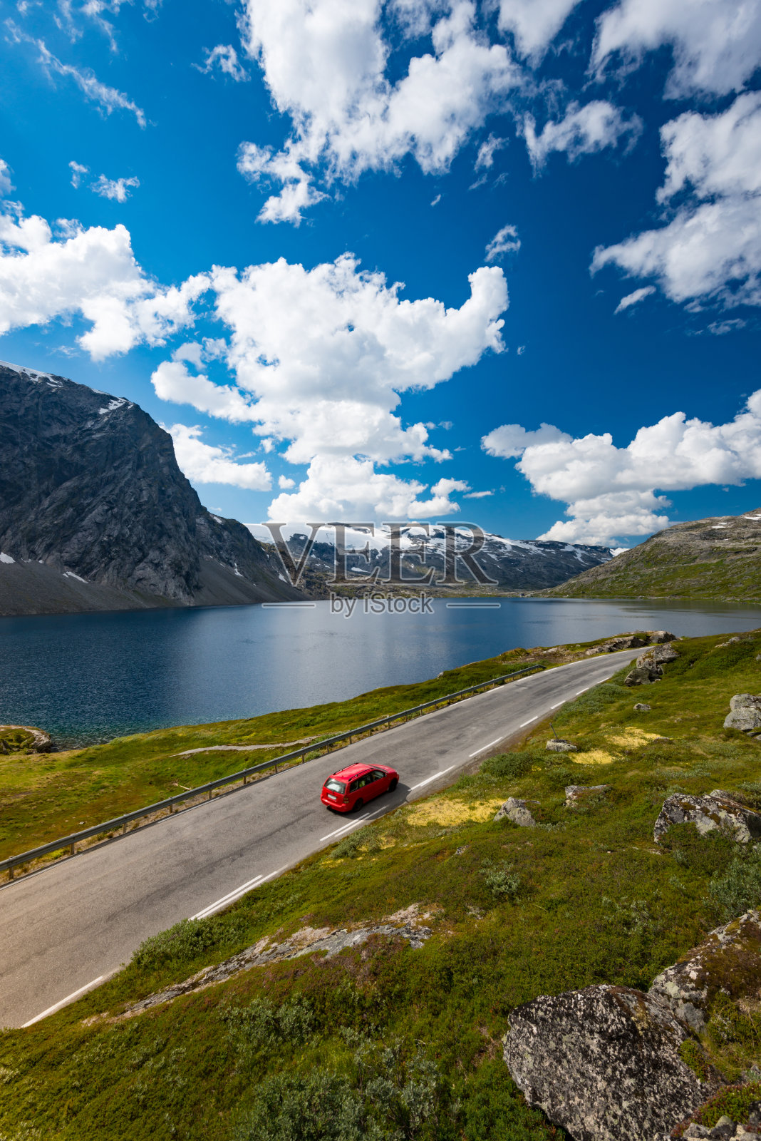 欧洲挪威山区的一辆红色轿车。穿越斯堪的纳维亚半岛的汽车旅行。蓝色多云的天空和湖的背景。照片摄影图片
