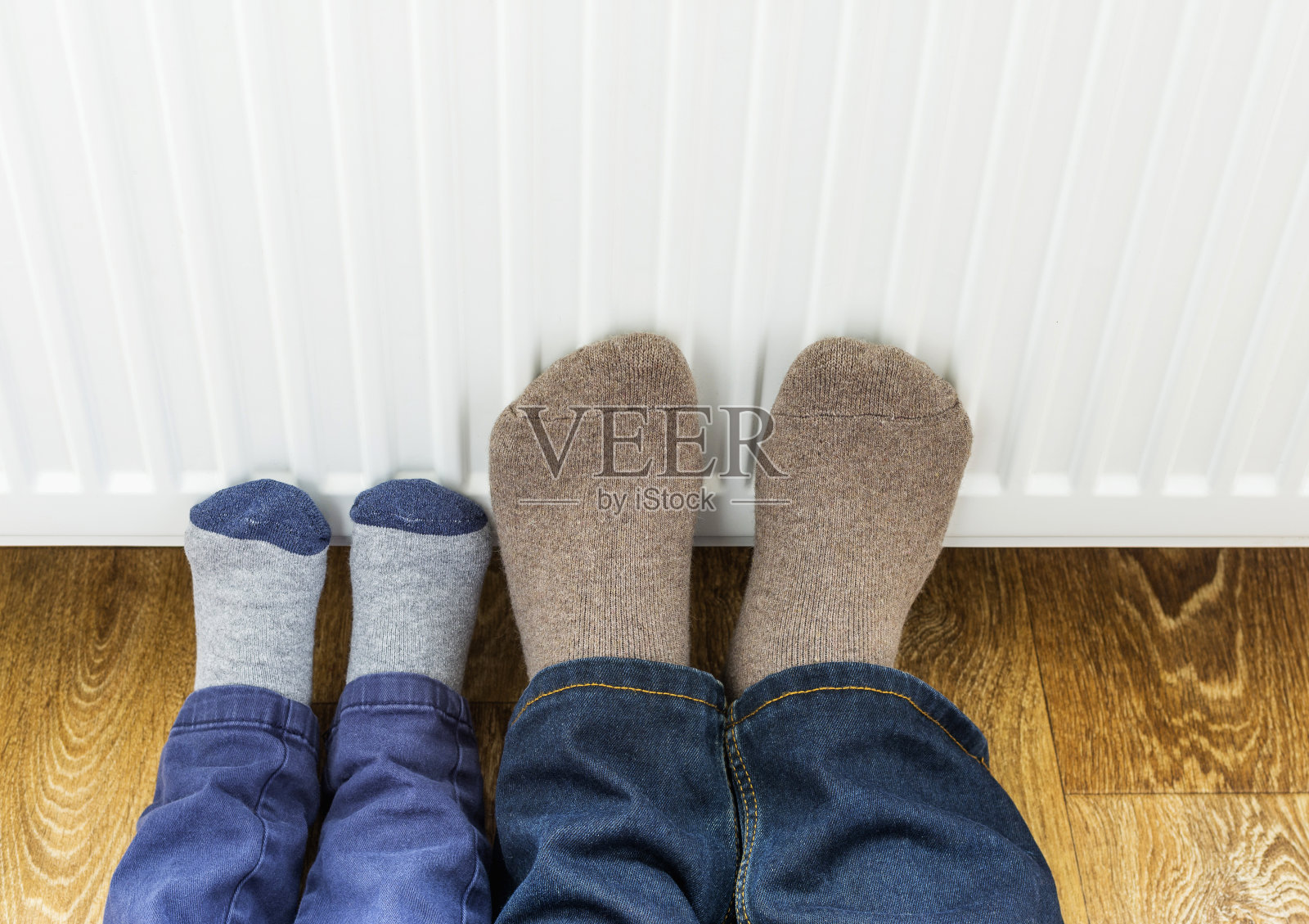 父子俩穿着冬天的羊毛袜子，在暖气片旁暖脚。照片摄影图片