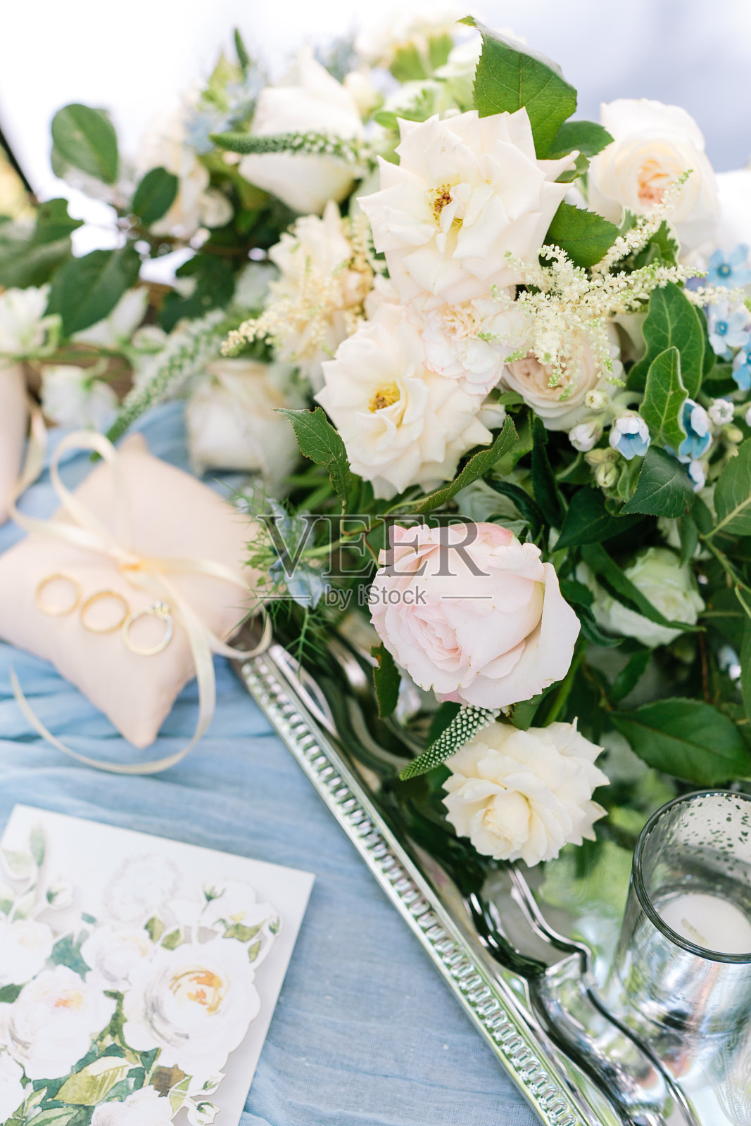 婚姻、感情、求婚观念。漂亮的新娘花束，优雅的奶油色和粉红色的玫瑰装饰着蓝色的小花，放在银光闪闪的托盘上，旁边还有戒指枕头照片摄影图片