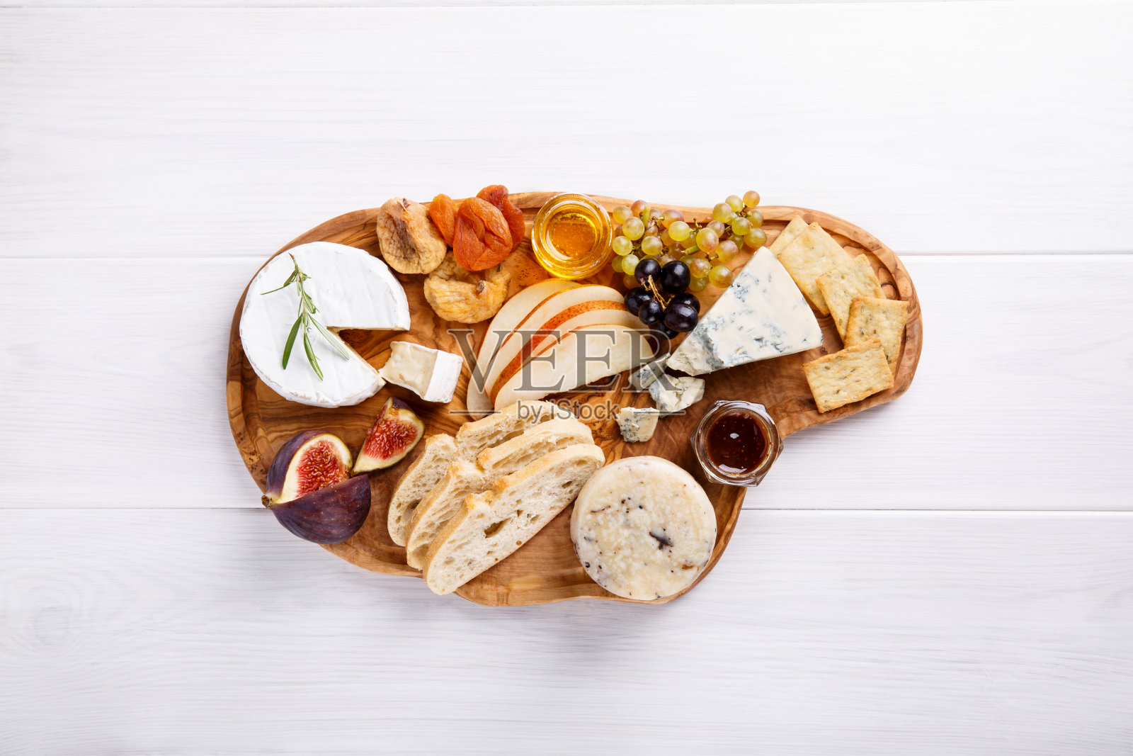 白色的桌子上放有蓝奶酪、布里干酪、松露硬奶酪、葡萄、无花果、梨、蜂蜜、饼干、干果和坚果。前视图。副本的空间。照片摄影图片