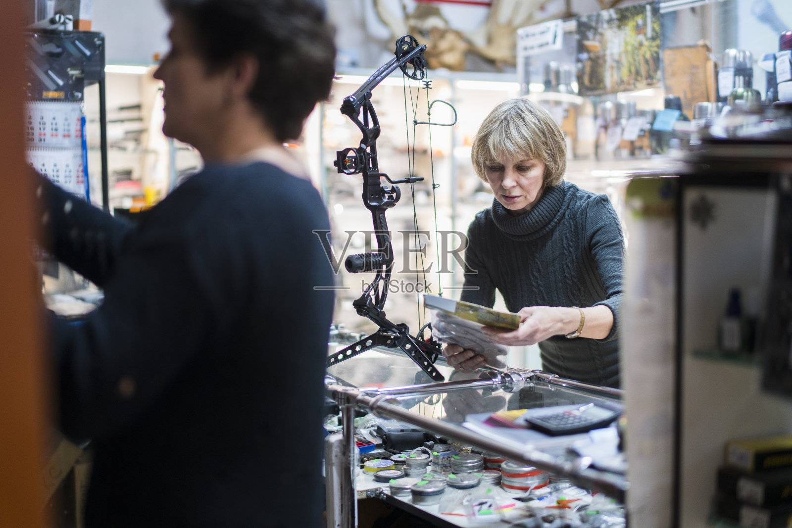 迷人的金发成熟，50岁的女人在小狩猎商店检查弓，与女售货员的协助。加里宁格勒，俄罗斯，东欧。照片摄影图片
