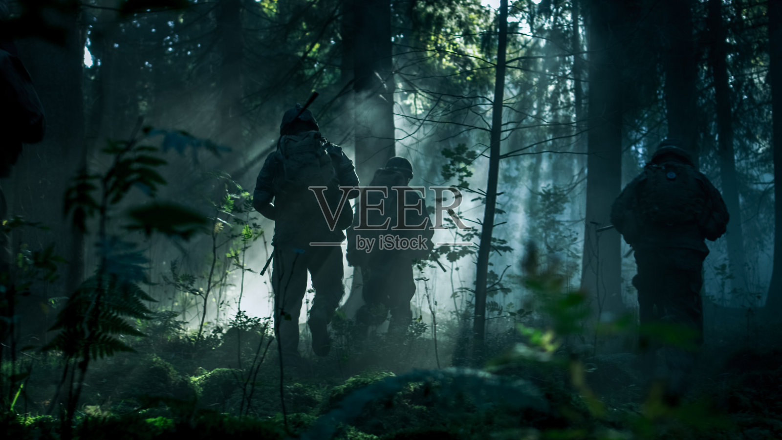 五名全副武装的迷彩服士兵小队执行一项侦察军事任务，步枪在射击位置。它们排成队形穿过茂密的黑暗森林。侧视图长镜头。照片摄影图片