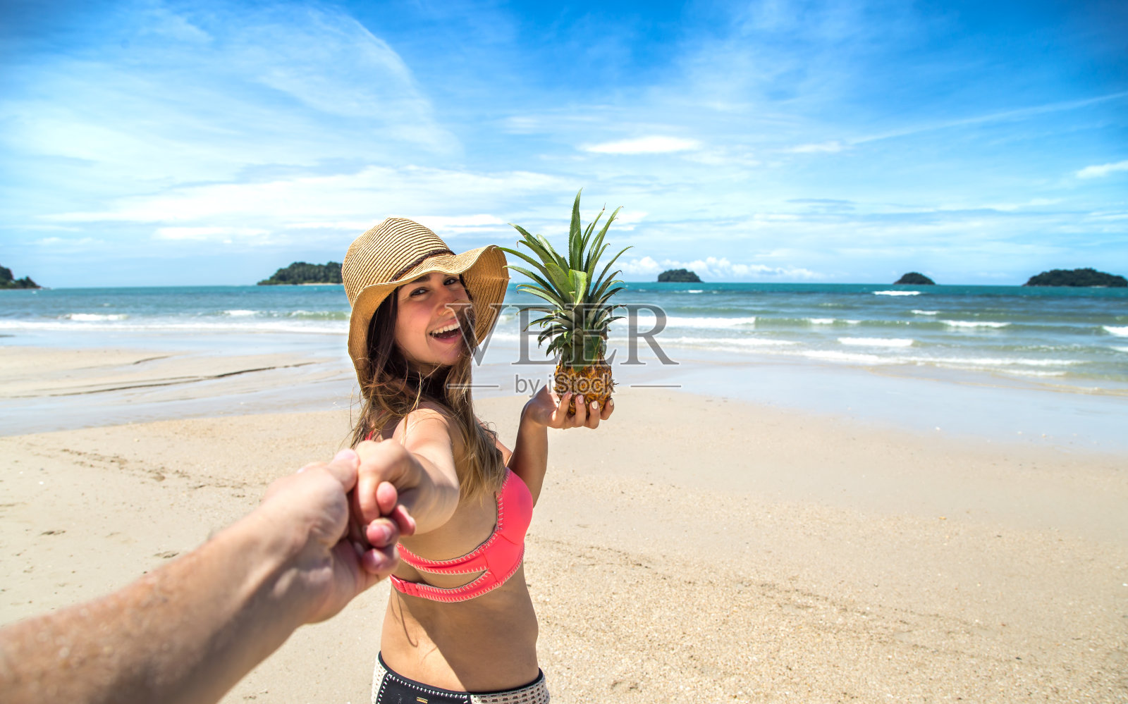 美丽的女孩穿着泳衣和菠萝走在海滩上，牵着男孩的手照片摄影图片