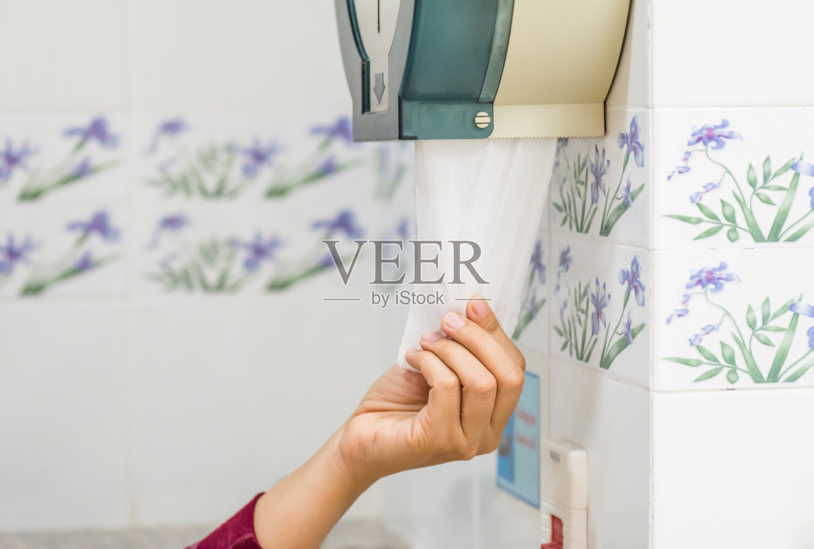 在以白色和蓝色为背景的洗手间里，一位女士从纸巾盒中拿出一张白色的纸巾。照片摄影图片