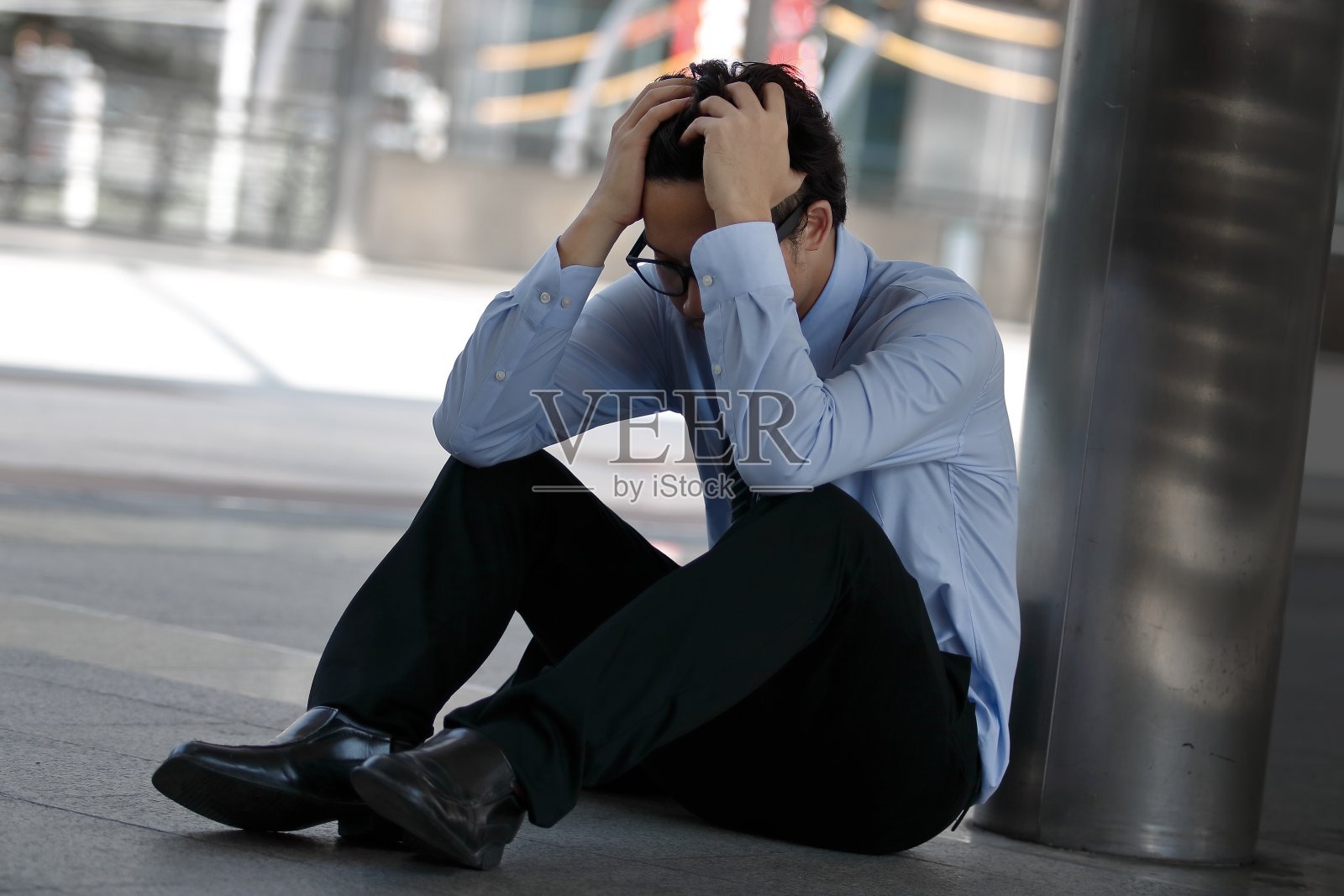沮丧而紧张的年轻亚洲男子用手捂着脸，坐在人行道上办公室的地板上，感觉工作很累照片摄影图片
