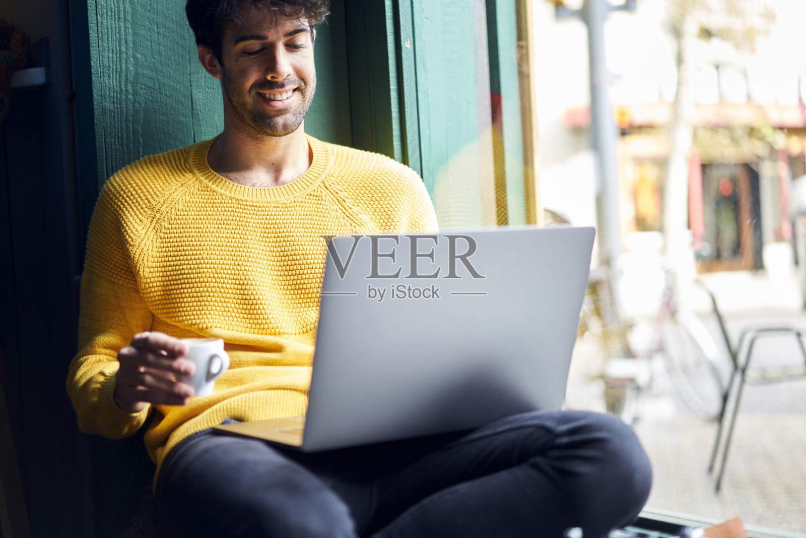 年轻英俊的男性自由职业者，为IT公司编写数字设备的程序，愉快地坐在咖啡杯和连接wifi的笔记本电脑里完成工作照片摄影图片