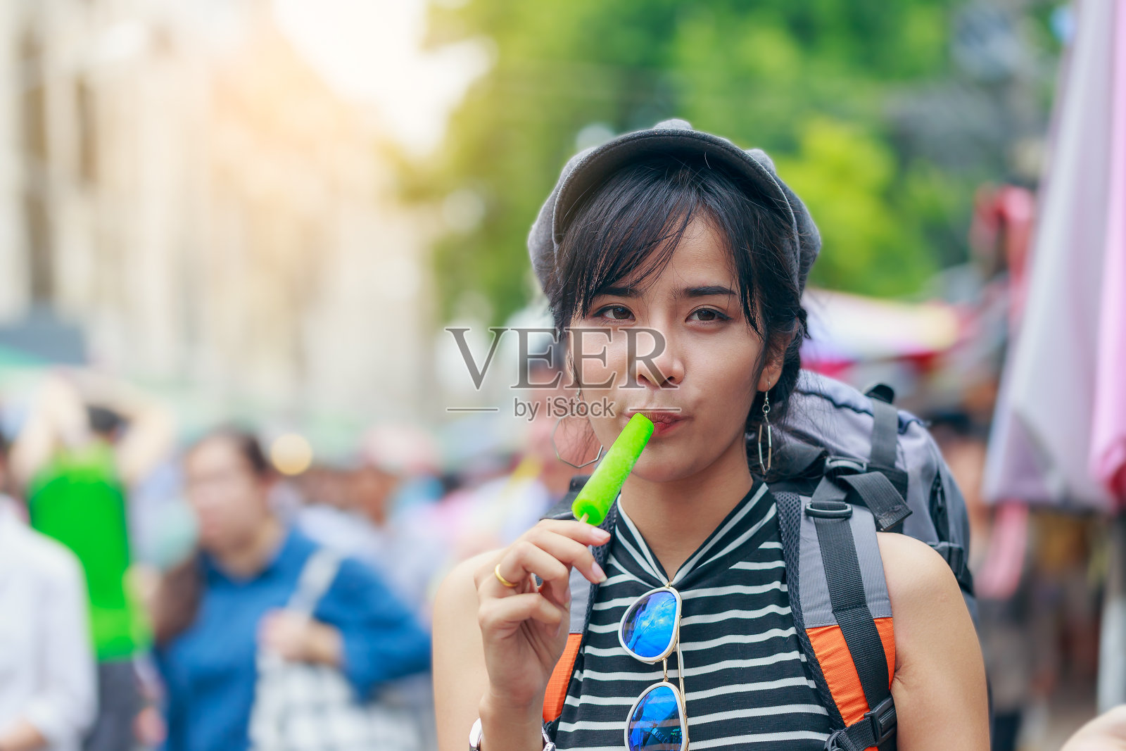 年轻的亚洲女性旅行者背着背包，在当地的市场街上吃冷饮照片摄影图片