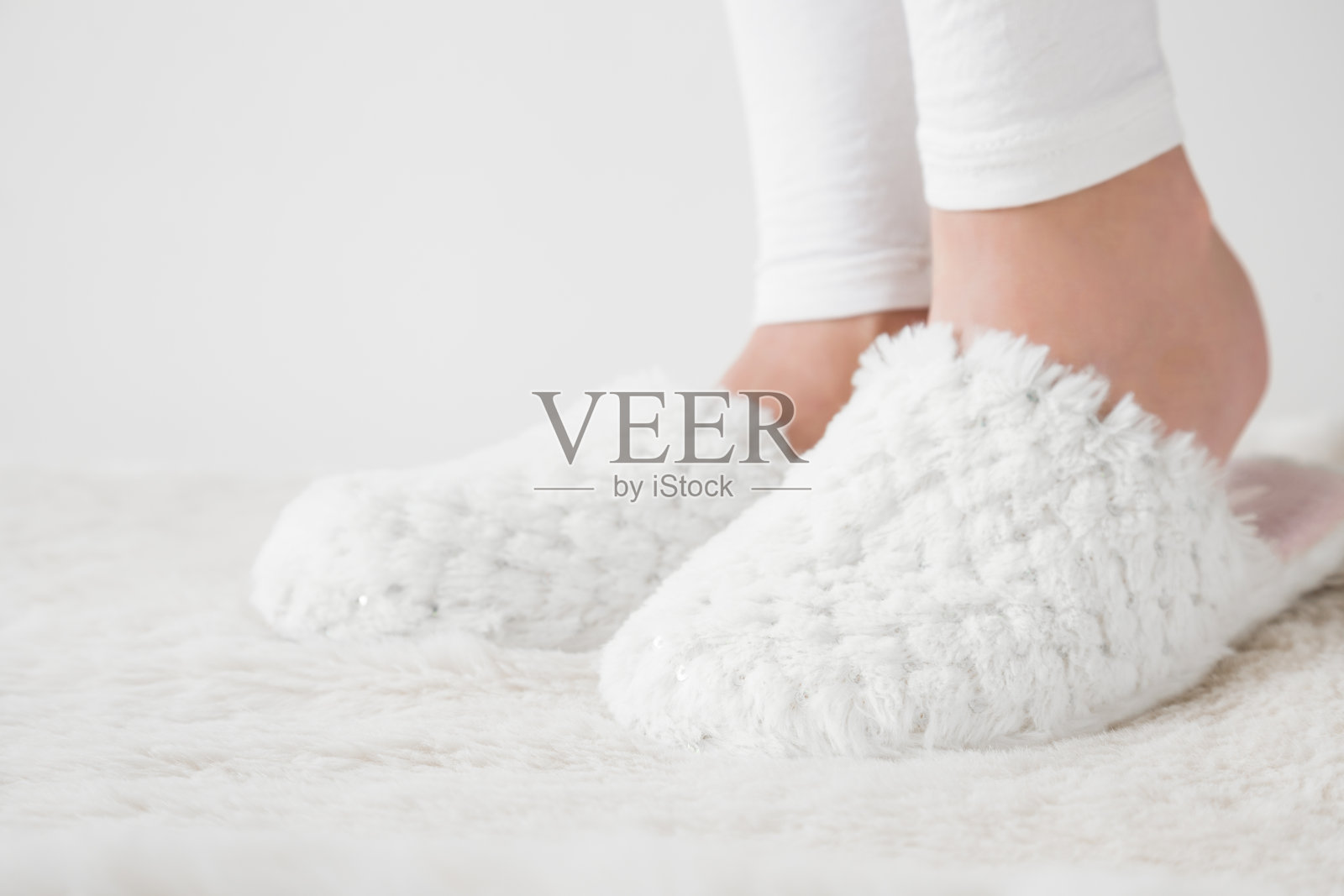 美丽，年轻女子的腿白色，柔软，温暖的拖鞋在蓬松的垫子在卧室早上醒来后。休息日在家休息。照片摄影图片