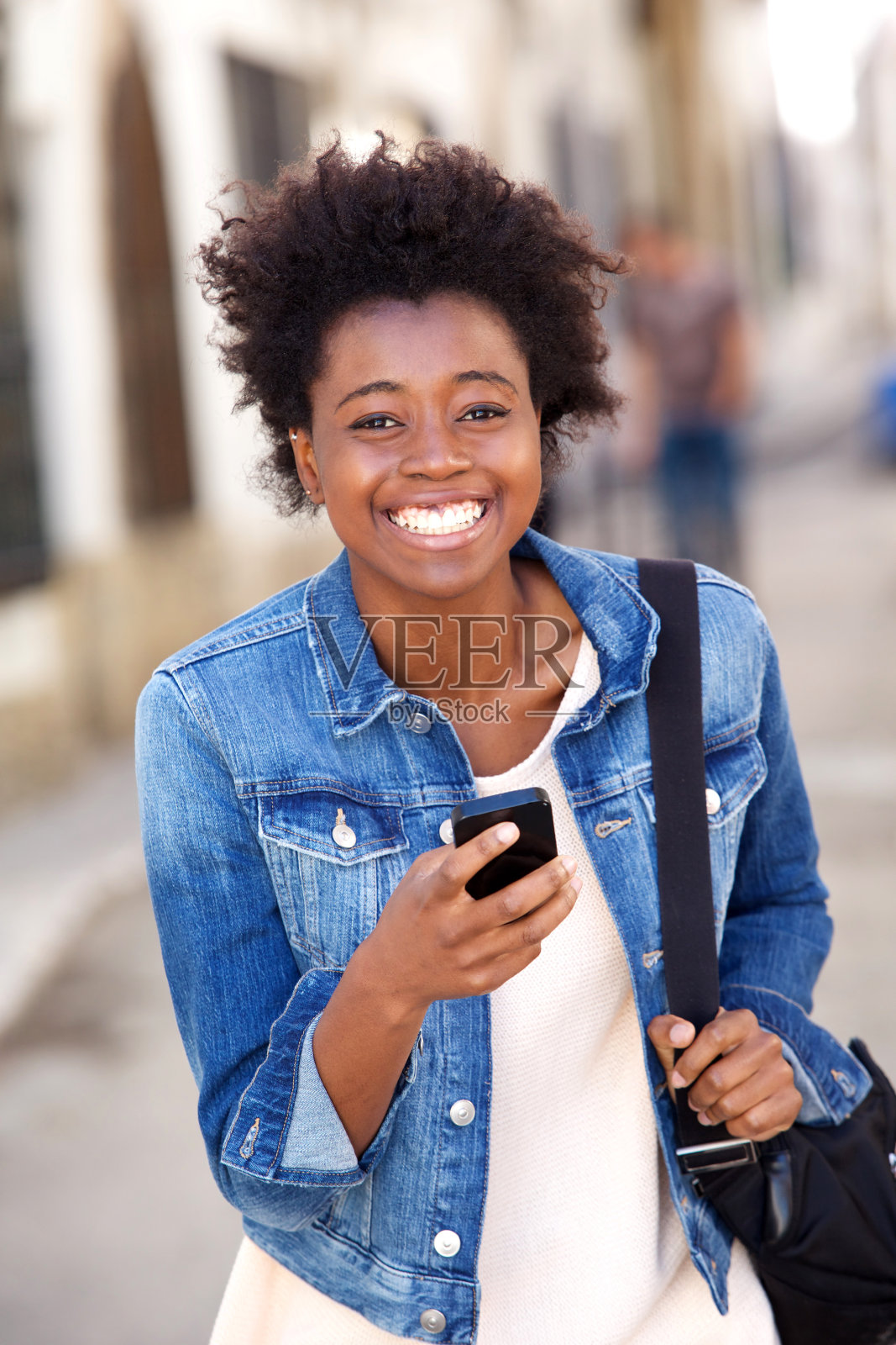 微笑的非洲女人拿着手机走在外面照片摄影图片