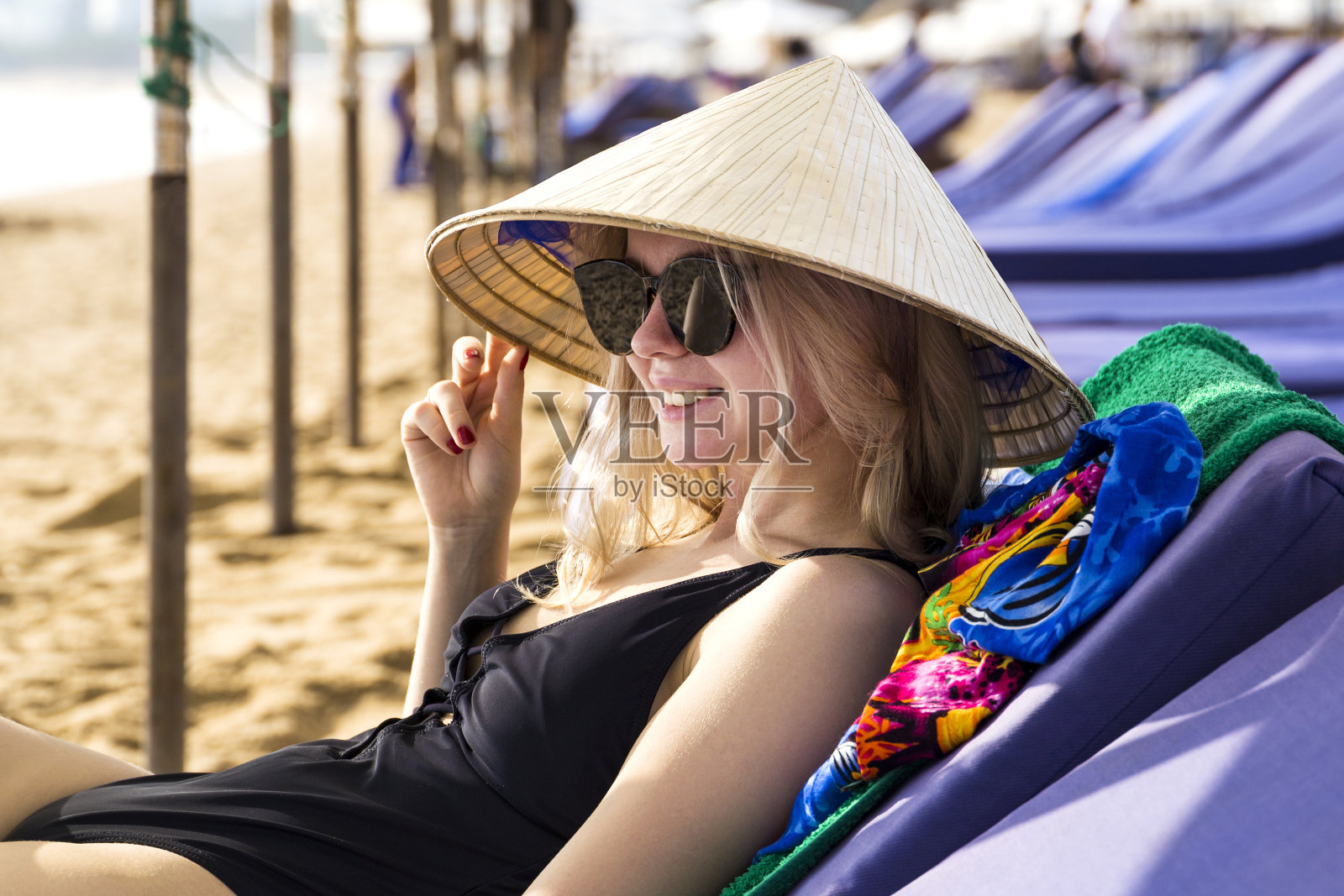 年轻美丽的女孩戴着传统的亚洲锥形帽子坐在海边的海滩上照片摄影图片