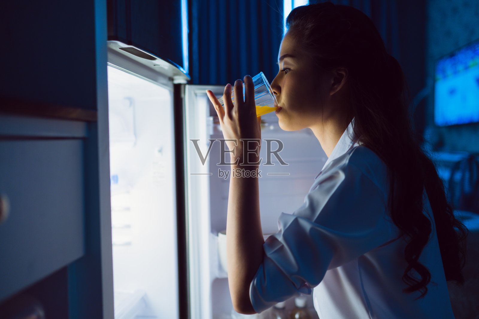 亚洲女性晚上打开冰箱，喝橙汁。照片摄影图片