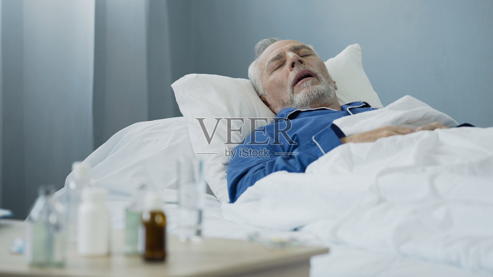 一位老人躺在病房的床上，抗生素放在桌子上照片摄影图片