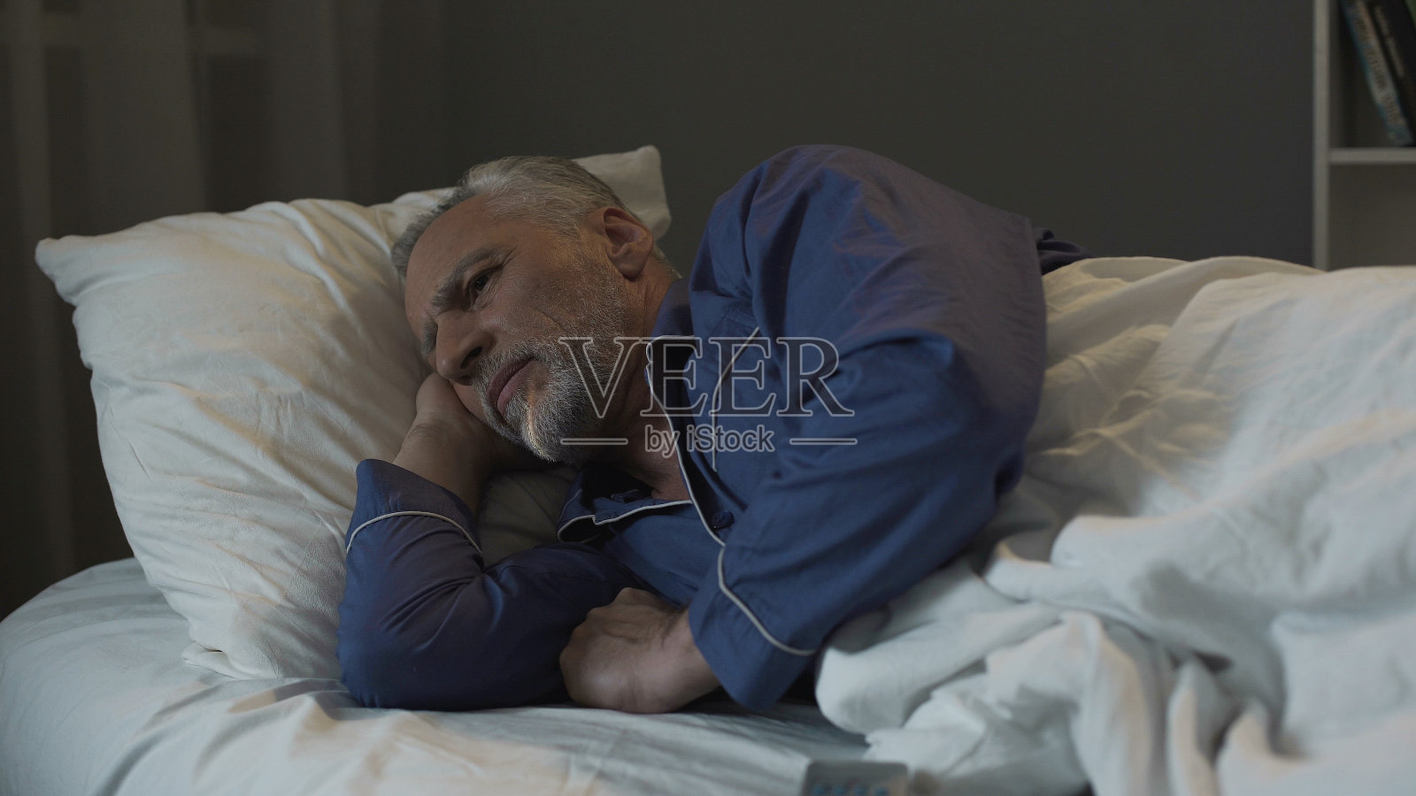 头发花白的男人躺在床上，饱受失眠、抑郁和健康的折磨照片摄影图片