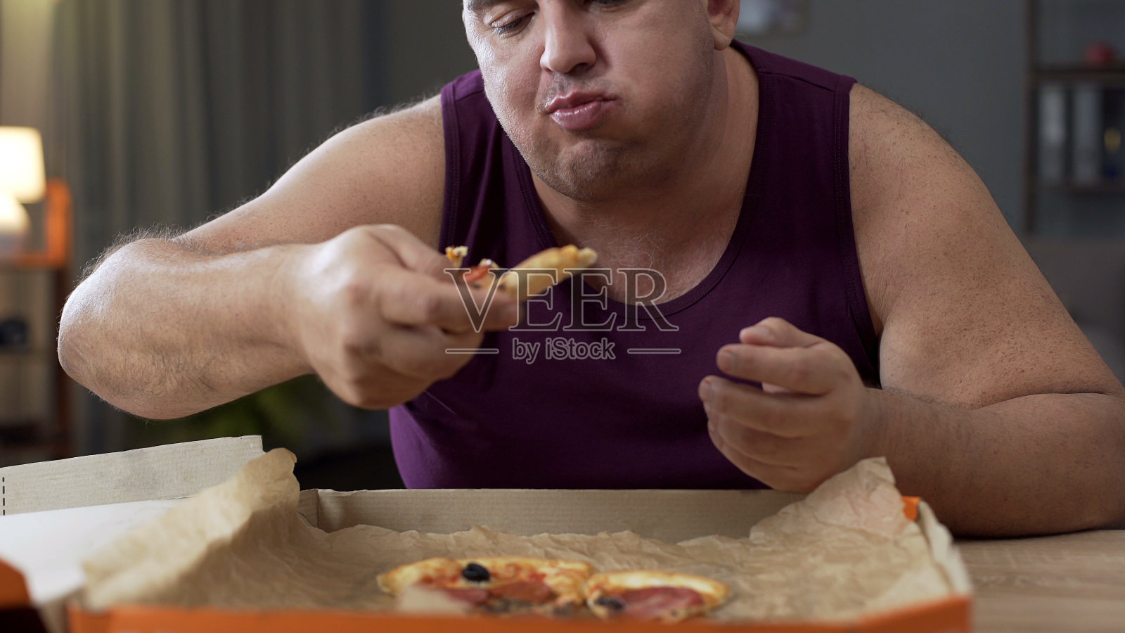 超重男性晚上喜欢吃披萨，对不健康的食物上瘾照片摄影图片