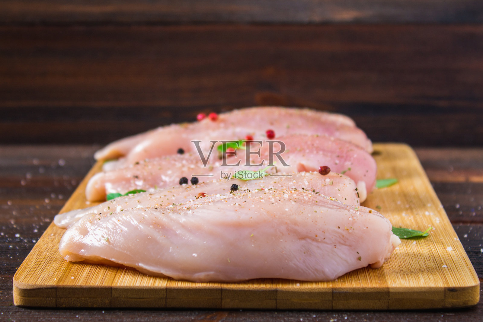 在木桌的背景下，一块切菜板上放着生鸡肉片。烹饪用的肉类配料。照片摄影图片