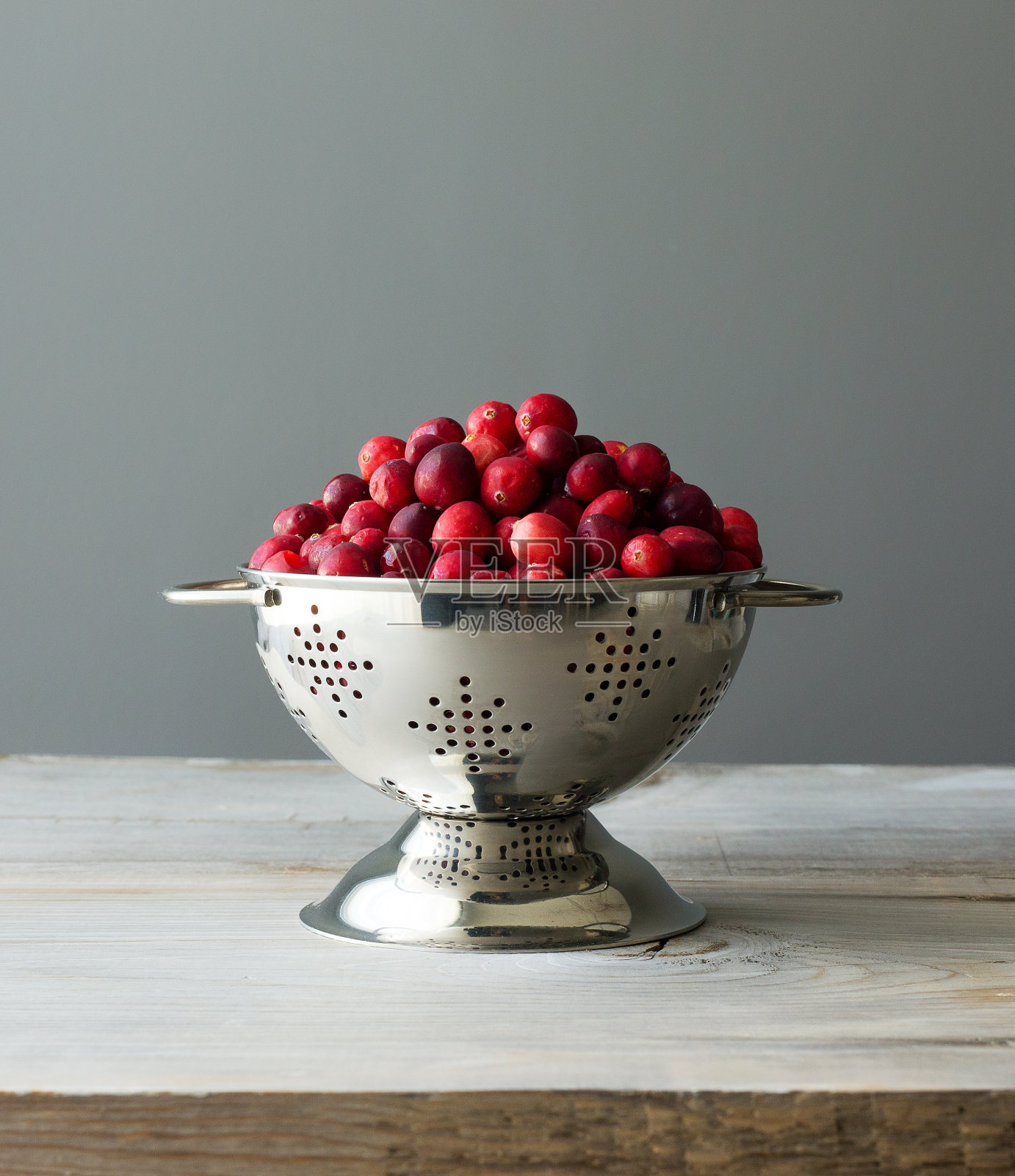新鲜的生蔓越莓放在一个小不锈钢滤锅里，背景是灰色。照片摄影图片