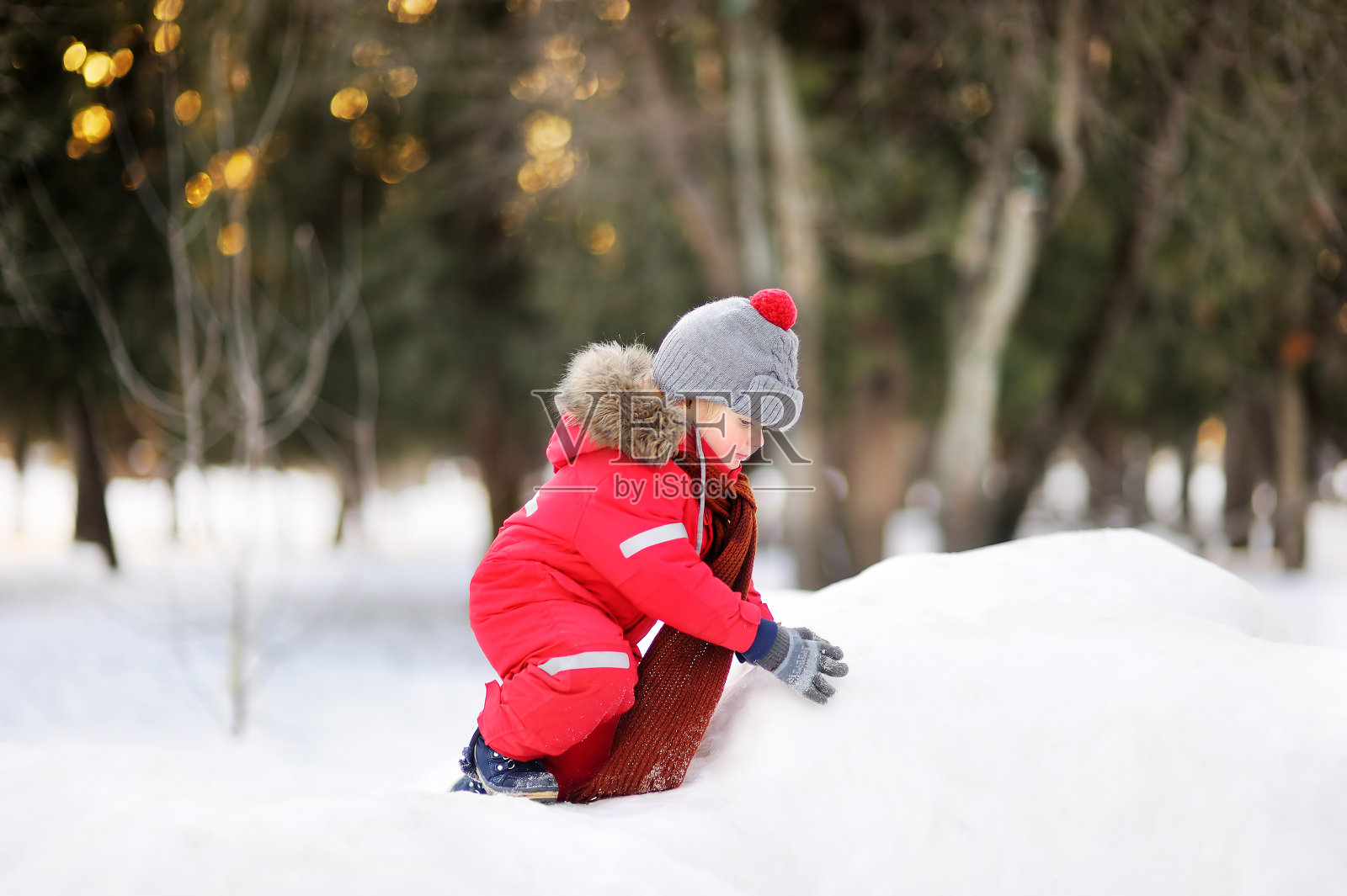 小男孩穿着红色的冬装和新鲜的雪玩照片摄影图片