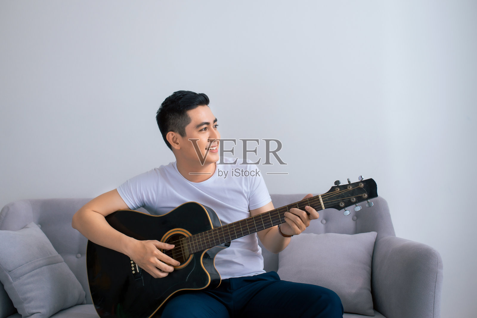 英俊的亚洲男人在家里的沙发上弹吉他照片摄影图片