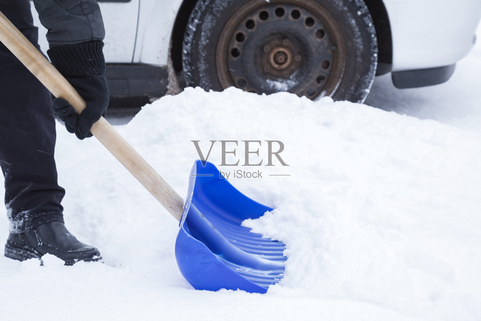 在冬天的一天，男人用蓝色的铲子清除汽车车轮前的积雪。冬季常规和问题概念。照片摄影图片