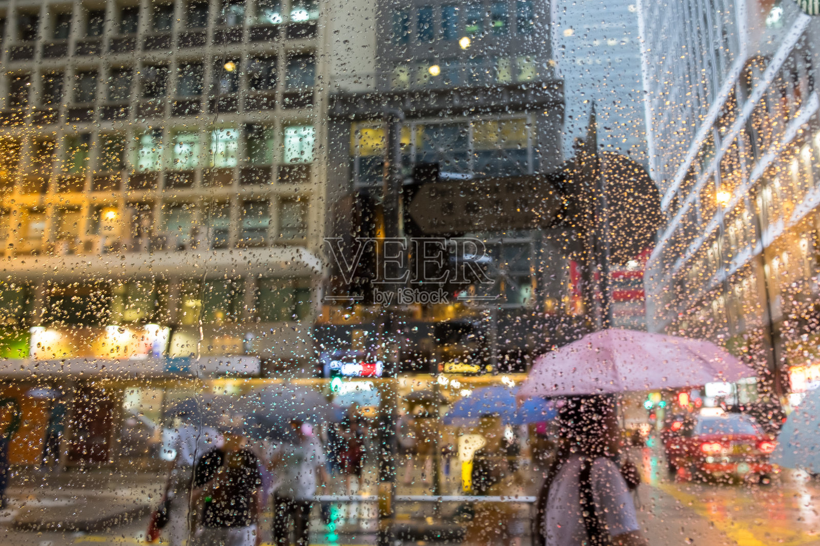 在雨中打着雨伞走在城市街道上的人们被模糊了。带着雨滴看窗外。照片摄影图片