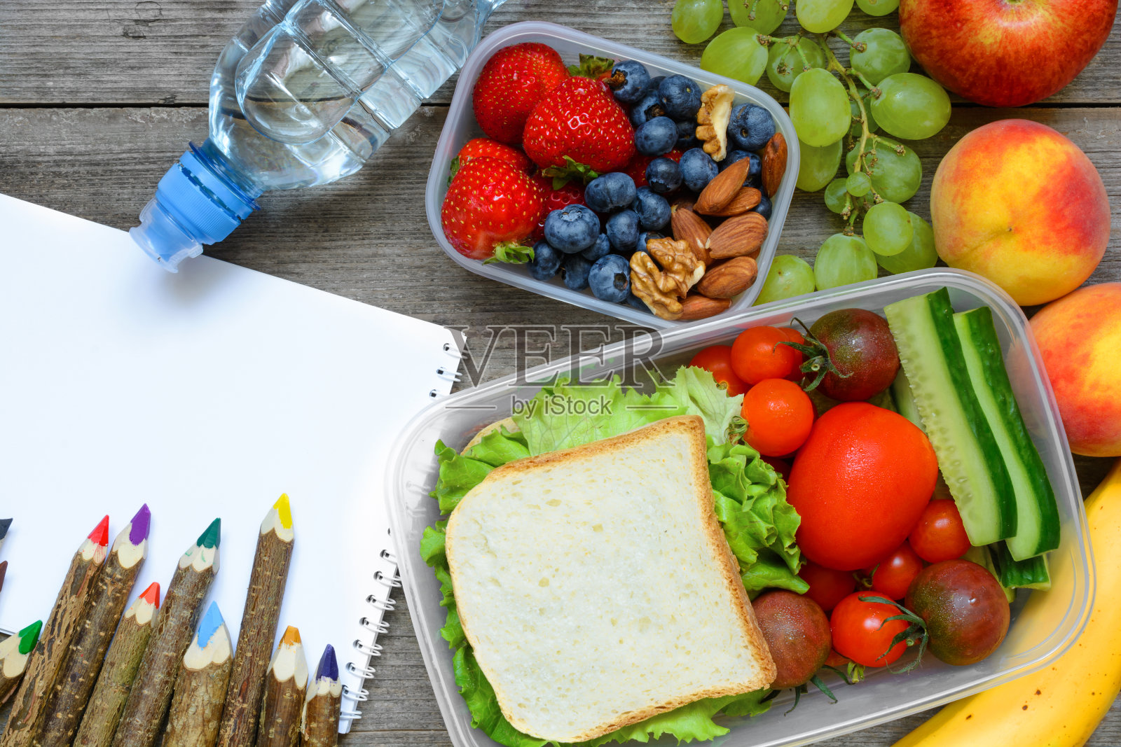 学校午餐盒里有三明治、水果、蔬菜和瓶装水，还有彩色铅笔和回学校的题字。照片摄影图片