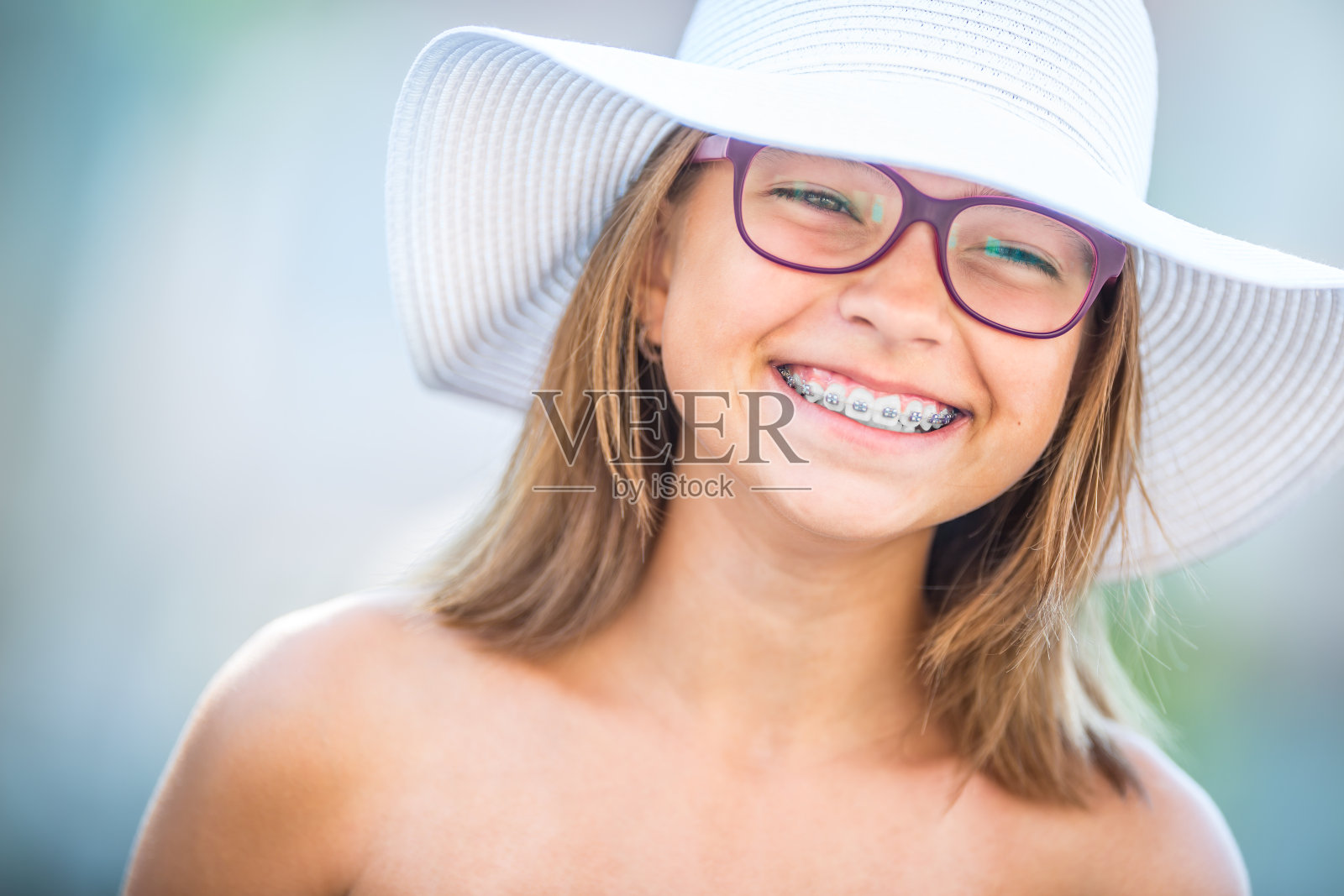 快乐的微笑女孩戴着牙套和眼镜。年轻可爱的白种金发女孩戴着牙套和眼镜照片摄影图片