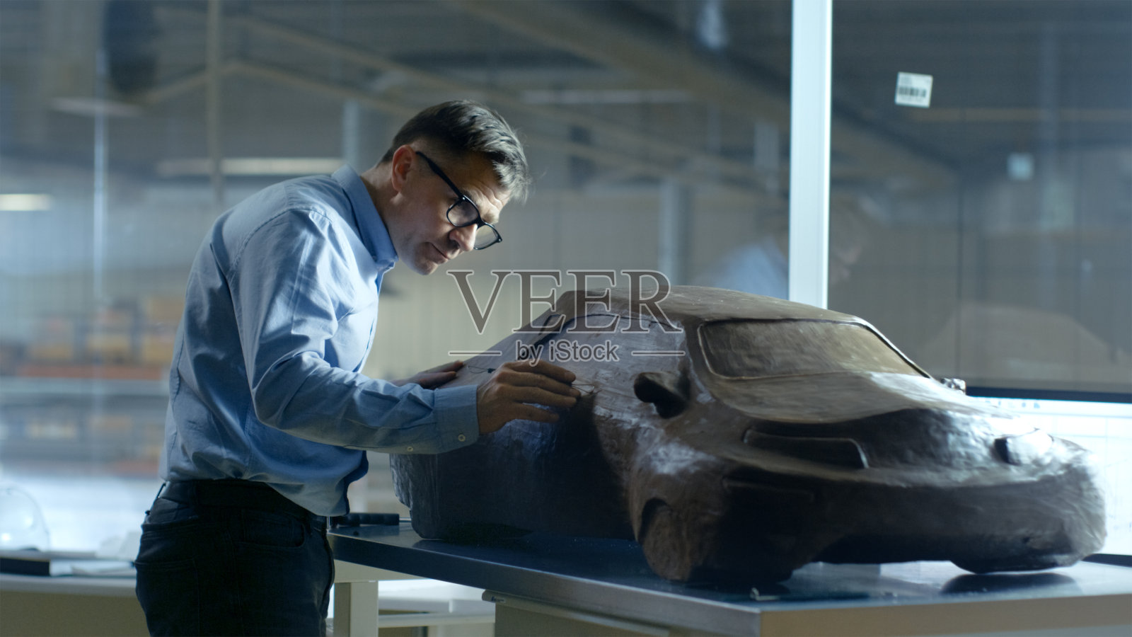 首席汽车设计师与Rake雕刻未来汽车模型从橡皮泥粘土。他在一家大型汽车厂的专门工作室工作。照片摄影图片