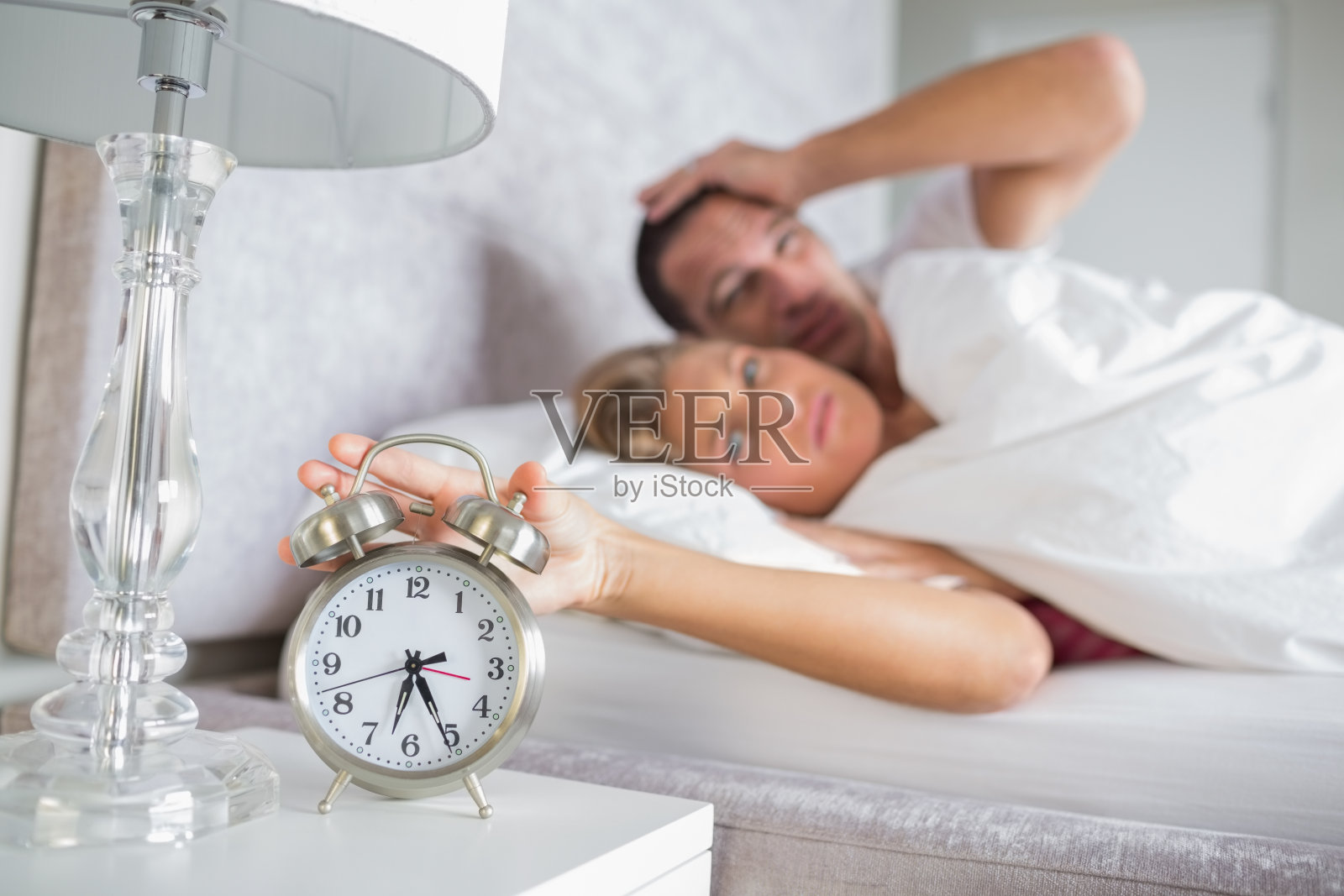 一对疲惫的夫妇早上看闹钟，女人关掉它照片摄影图片