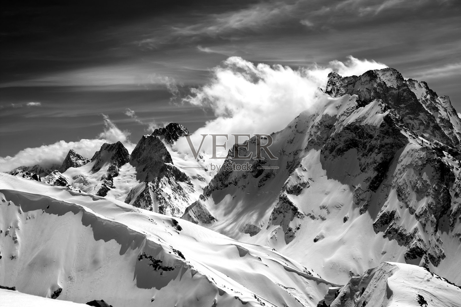 黑色和白色的冬季山与雪檐口和多云的天空在晴朗的日子照片摄影图片