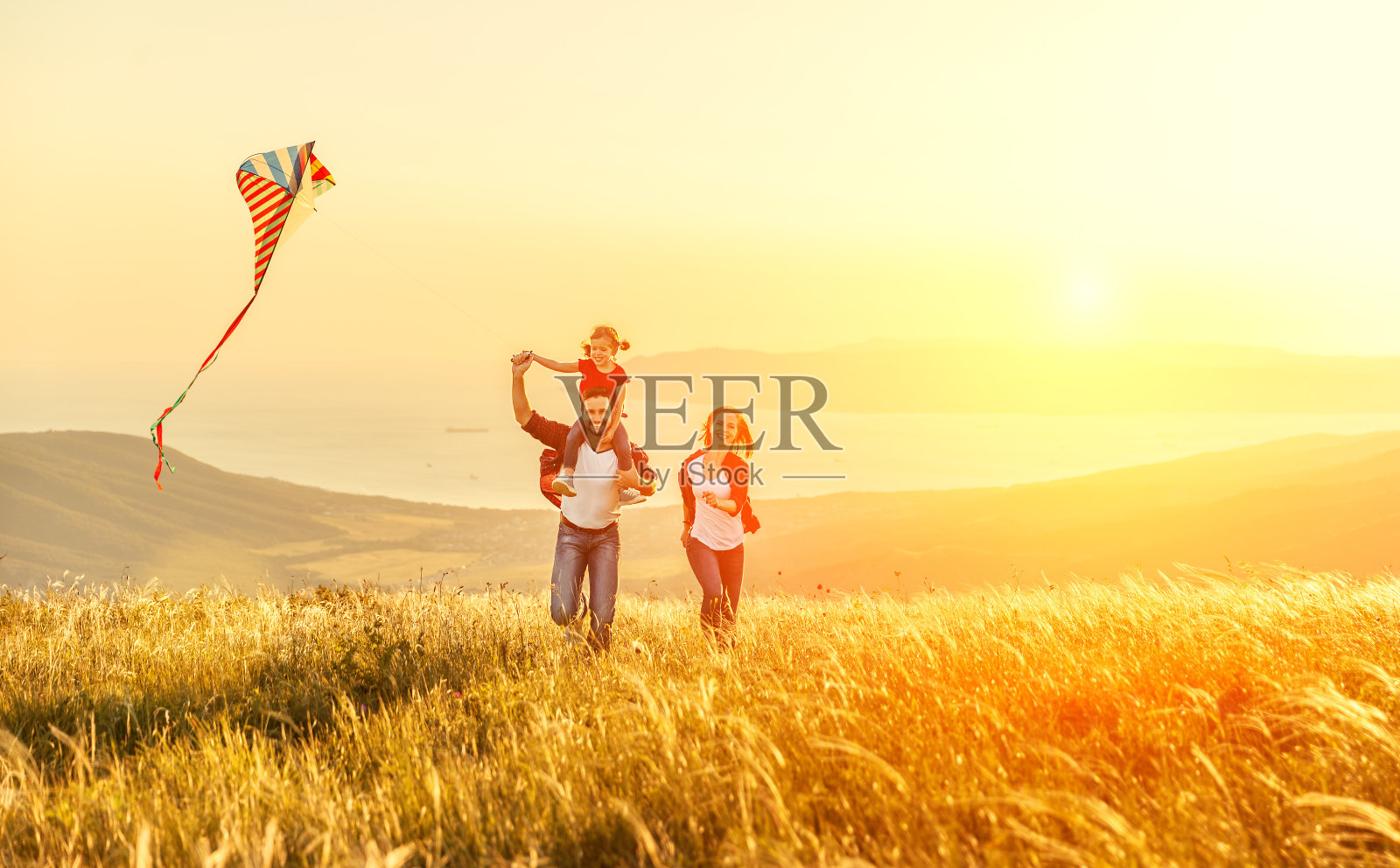 幸福的家庭，父亲母亲和孩子的女儿在自然放风筝在日落照片摄影图片