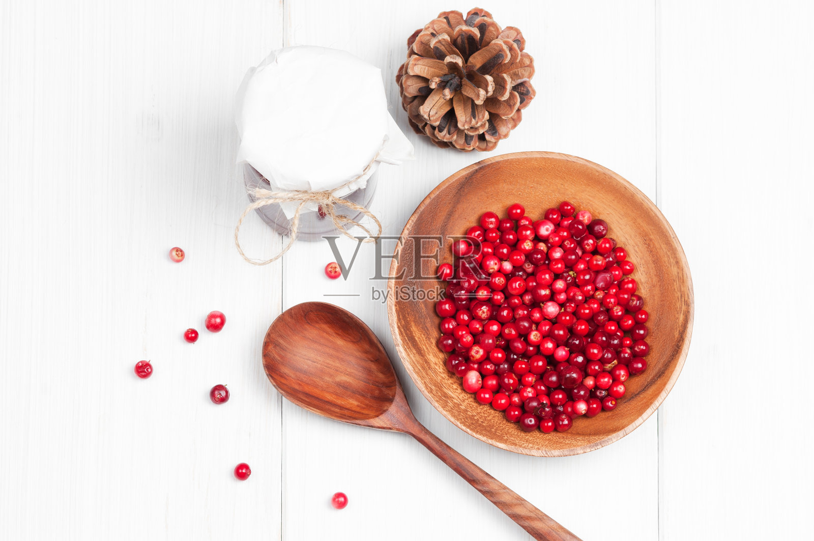 顶部平面视图:蔓越莓在木碗和果酱与勺子在白色表面照片摄影图片