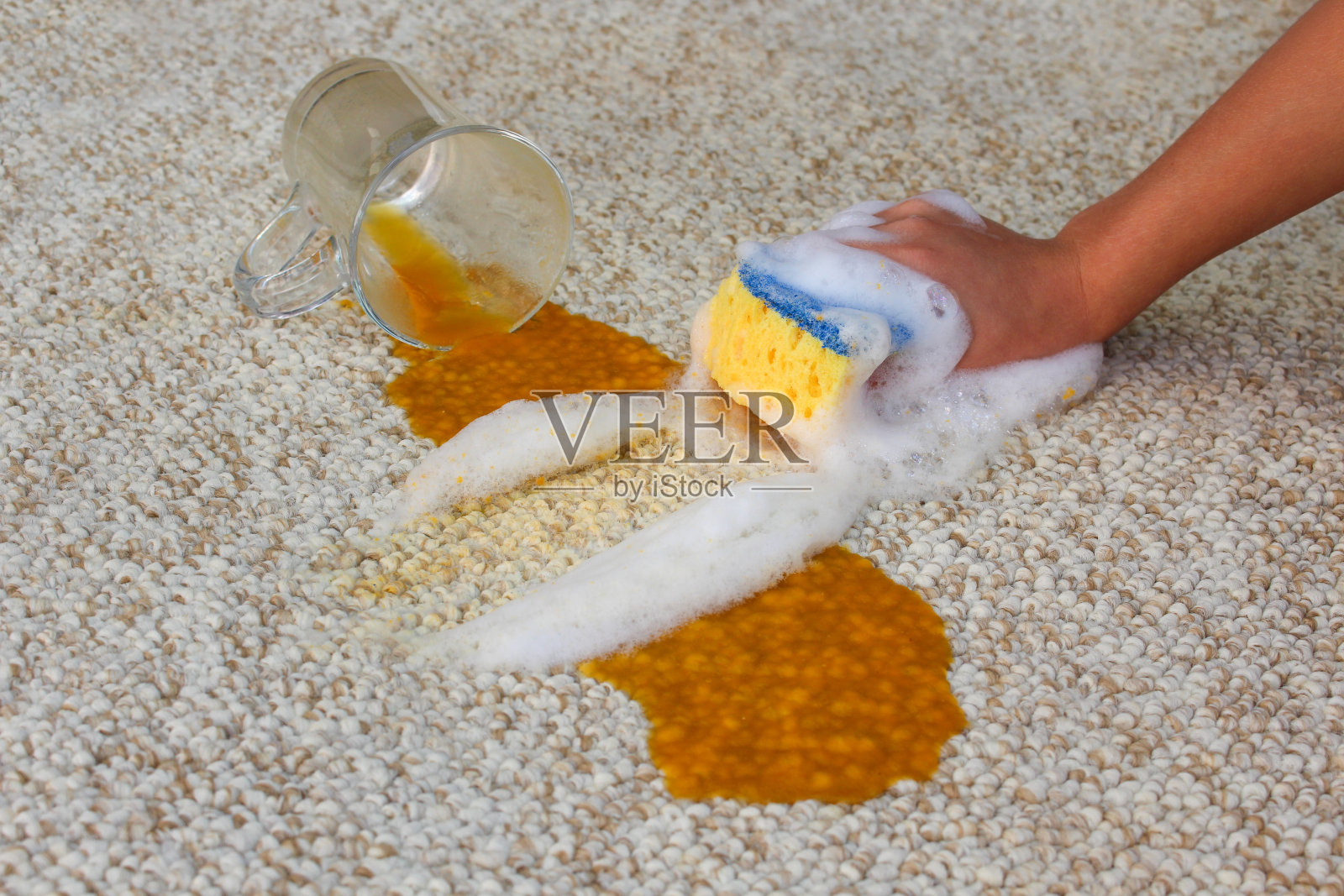 一杯果汁掉在地上，洒了一地。女人的手用海绵和洗涤剂清洗地毯。照片摄影图片