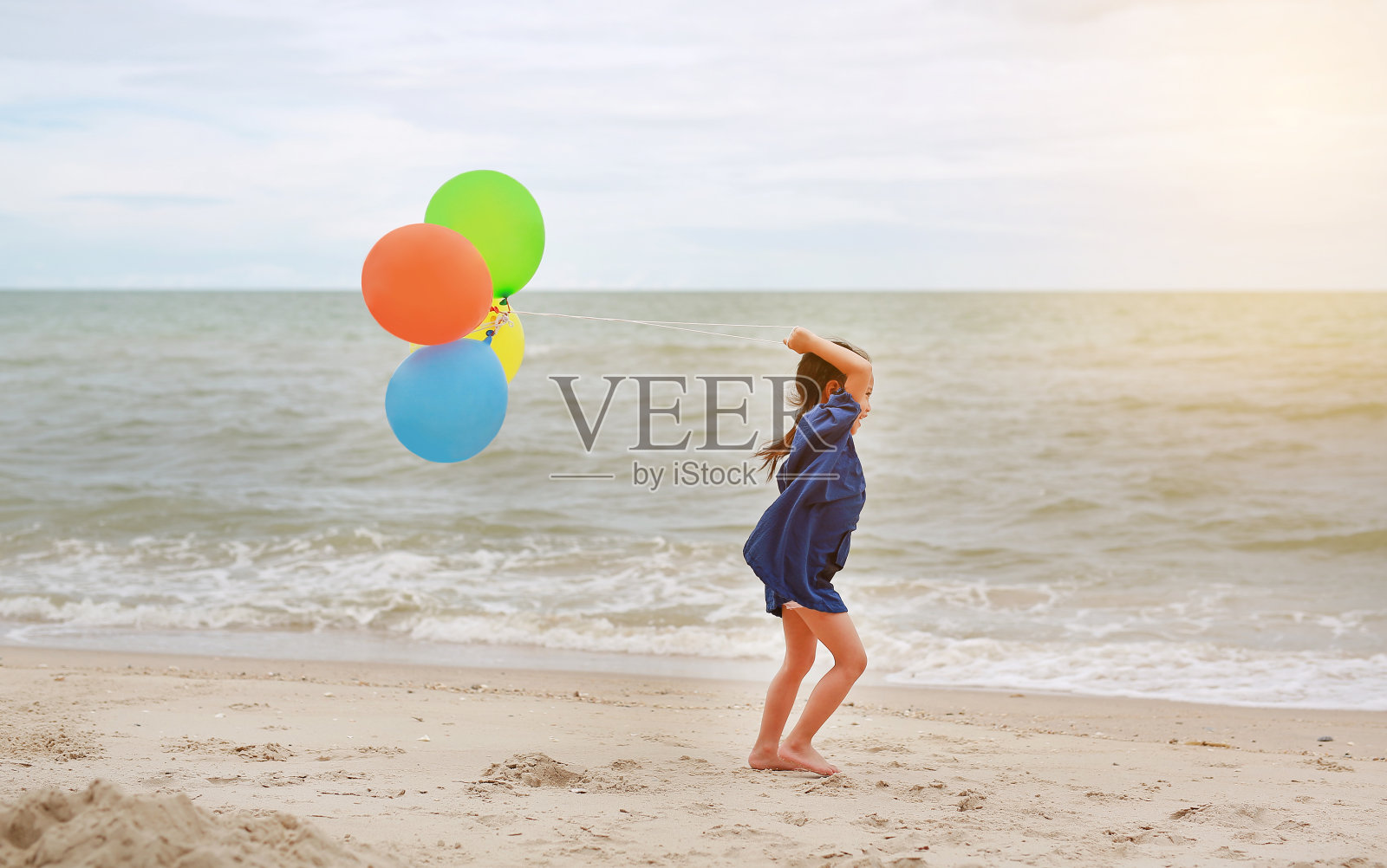 亚洲小女孩的肖像与阳光在海滩玩彩色气球。照片摄影图片