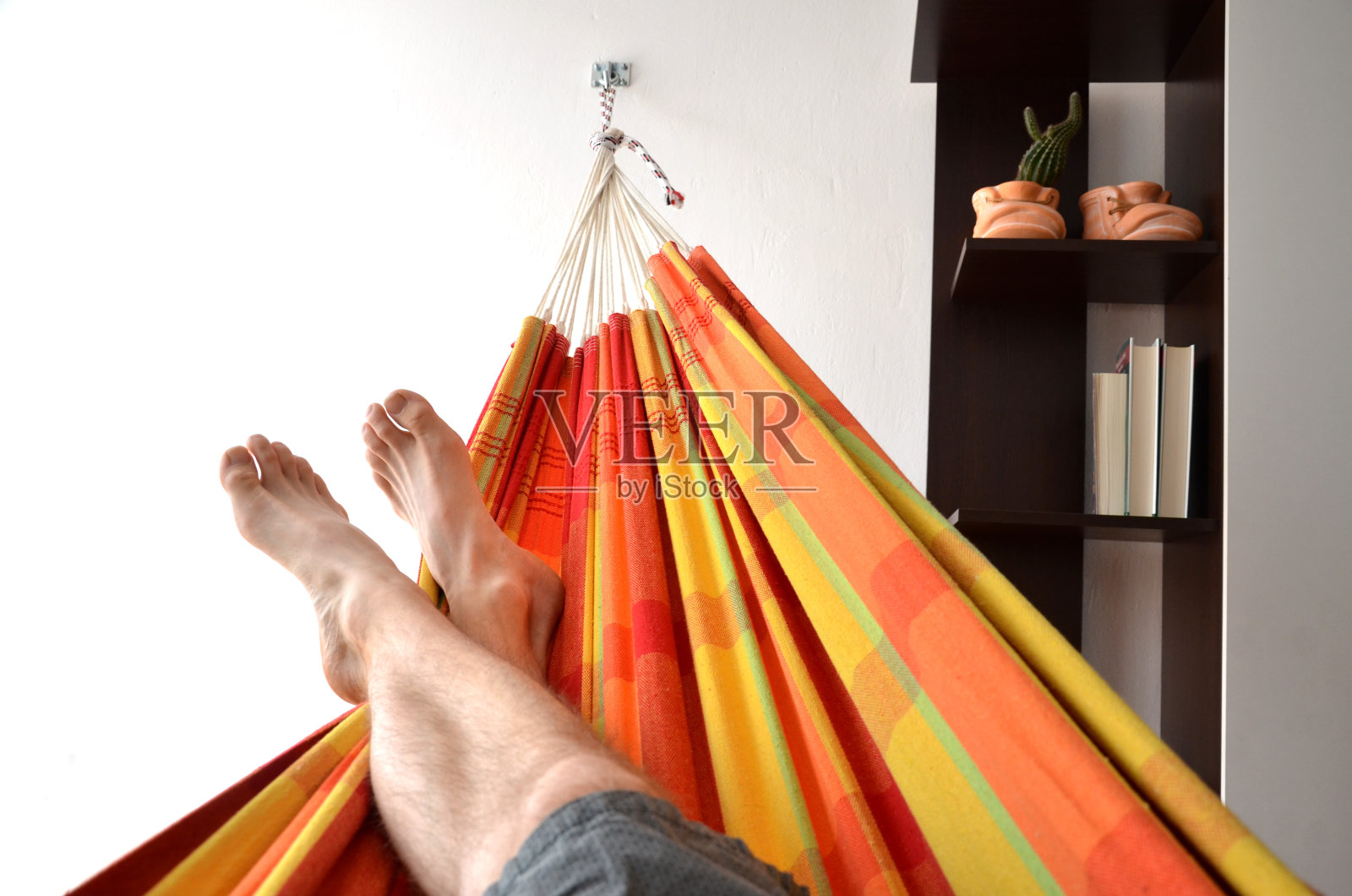 人的脚躺在明亮的吊床上，吊床附在室内墙壁上照片摄影图片