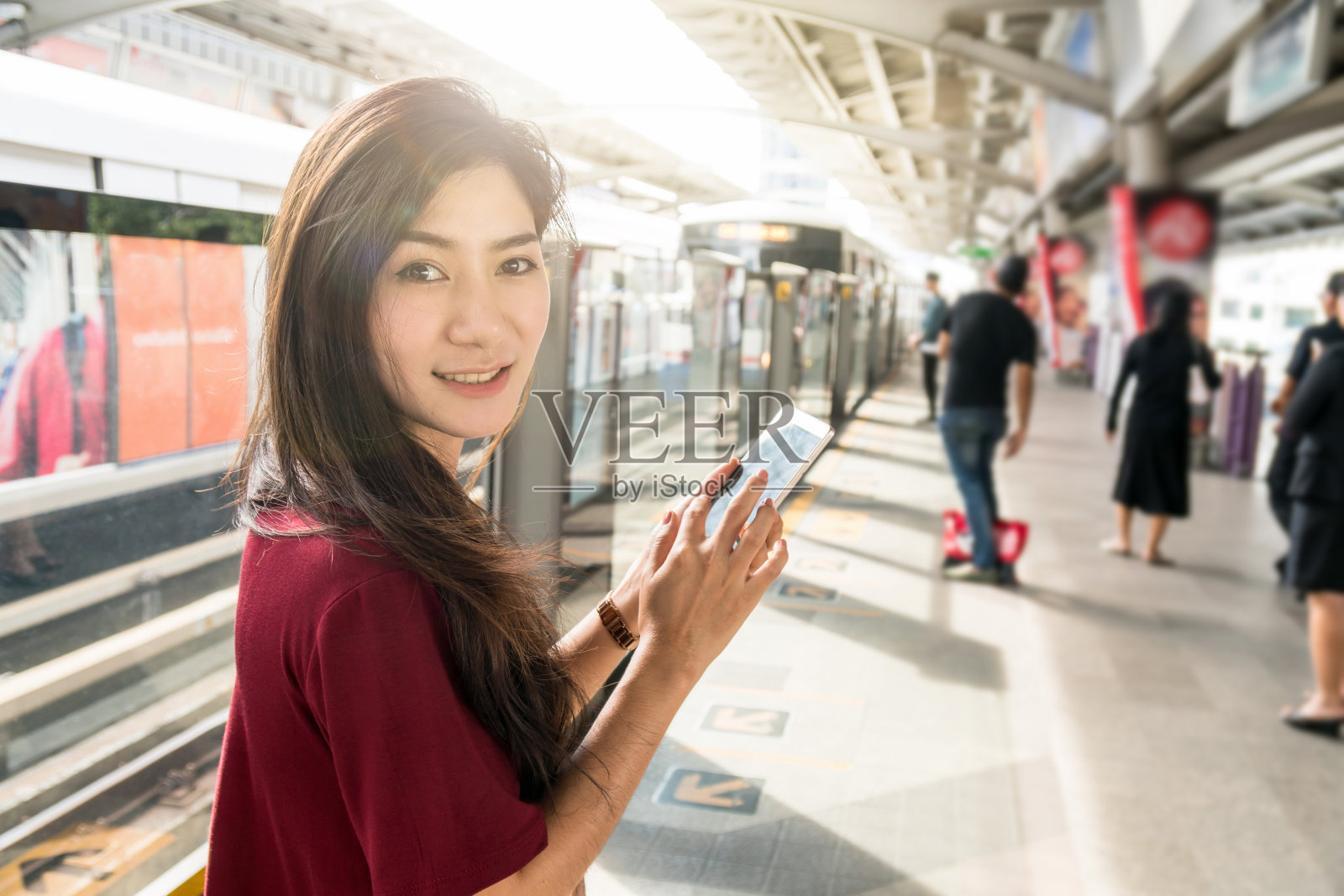 亚洲女性乘客穿着休闲套装，在BTS轻轨或捷运地铁上使用带镜头光斑的科技平板，在大城市旅行，生活方式和交通理念照片摄影图片