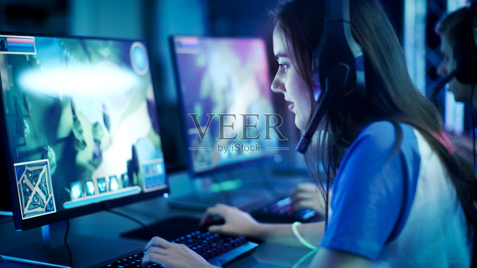 职业女性玩家在她的电脑上玩MMORPG/策略电子游戏。她参加网络游戏比赛，在家里玩，或在网吧玩。她戴着游戏耳机。照片摄影图片