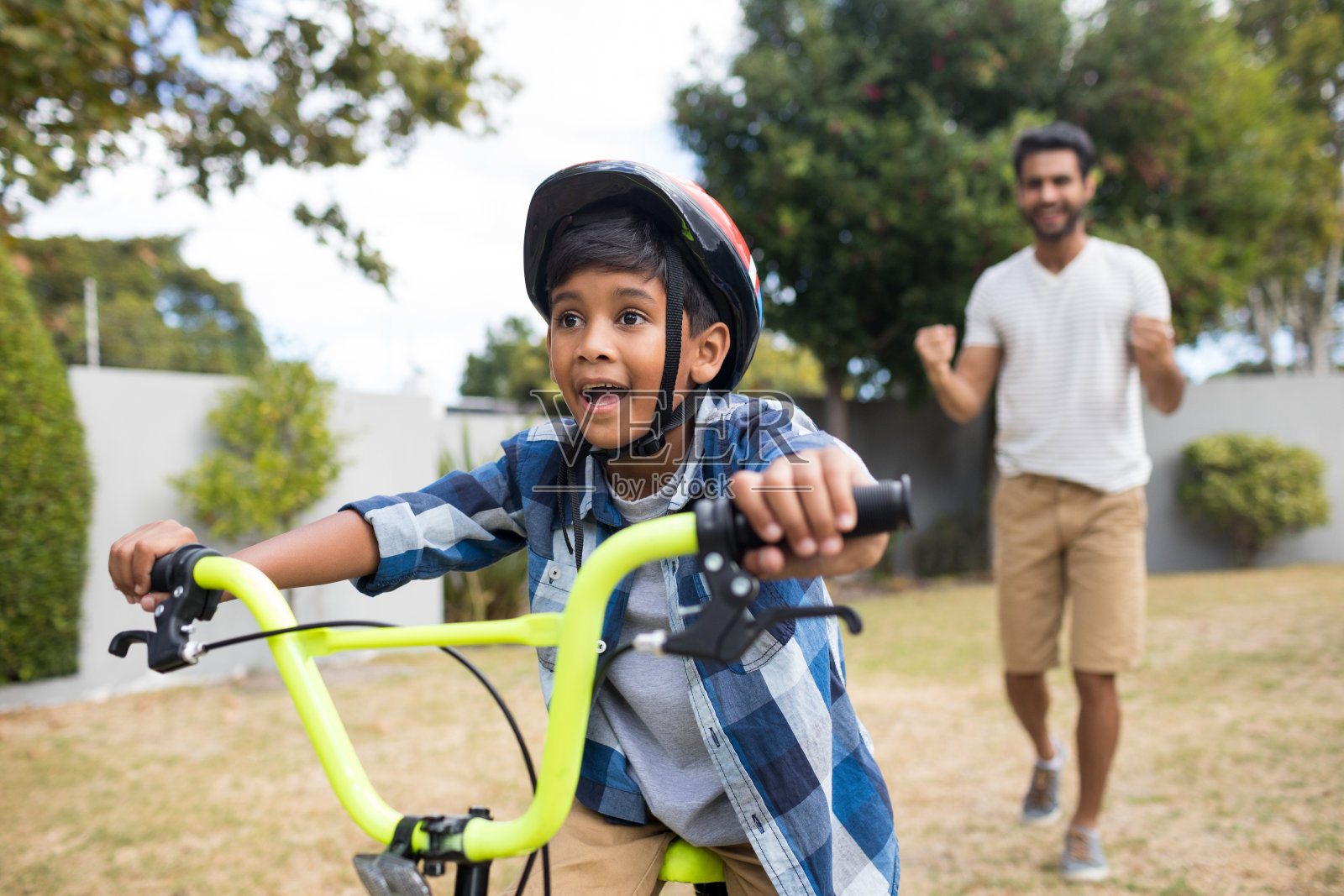 男孩骑着自行车，父亲站在后面照片摄影图片