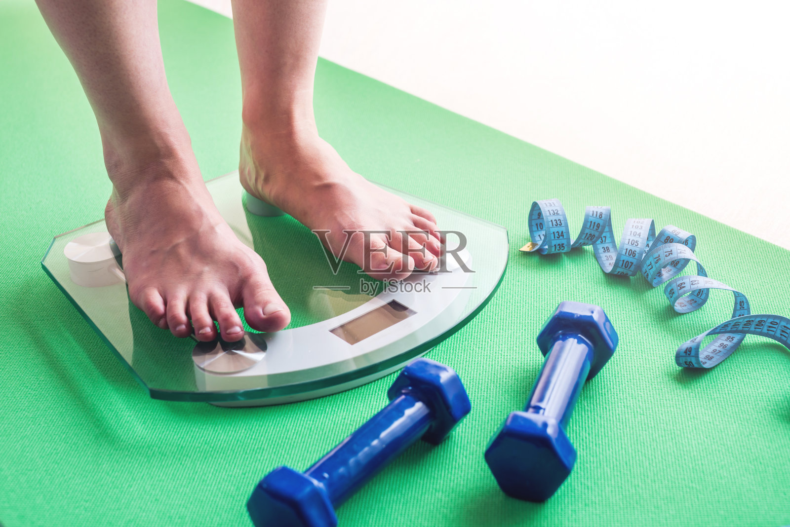 女性脚站在电子秤、哑铃和卷尺上。减肥和减肥的概念照片摄影图片