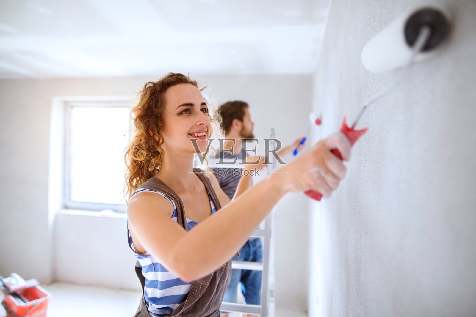一对年轻夫妇正在粉刷他们新房子的墙壁。照片摄影图片