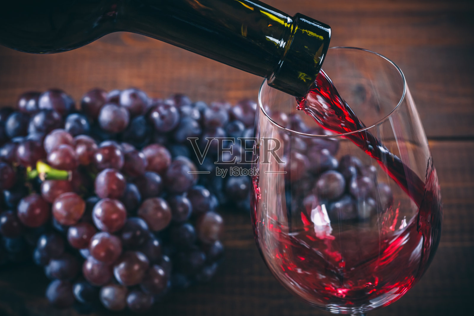 将红酒倒入玻璃杯中，以一串红葡萄为背景照片摄影图片
