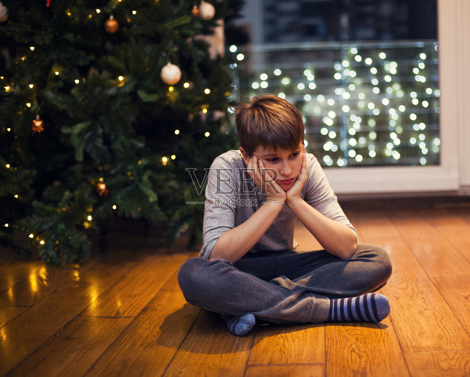 家里圣诞树旁的伤心男孩照片摄影图片