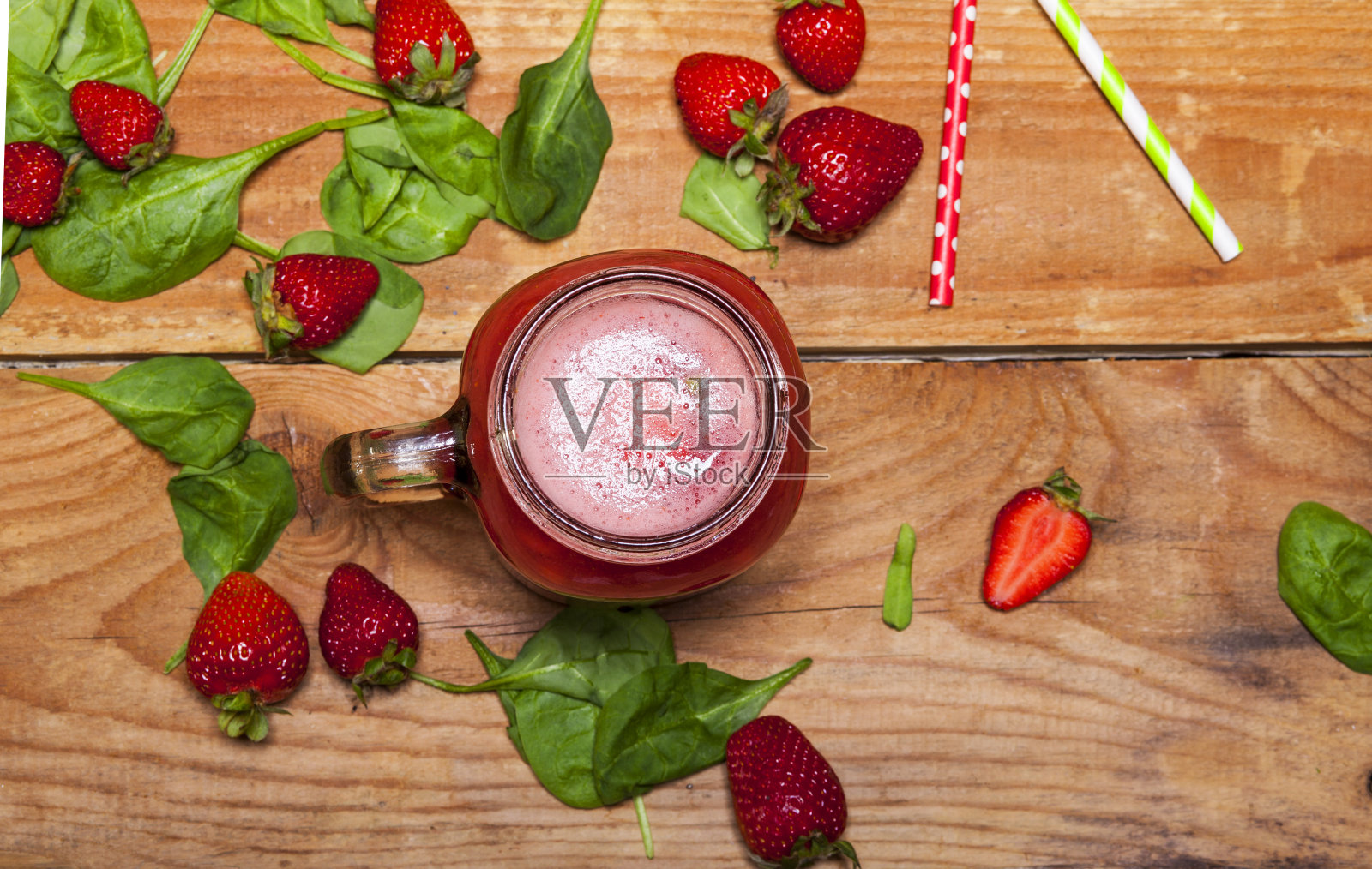 草莓冰沙或奶昔在一个罐子和菠菜叶子在木制的背景。照片摄影图片
