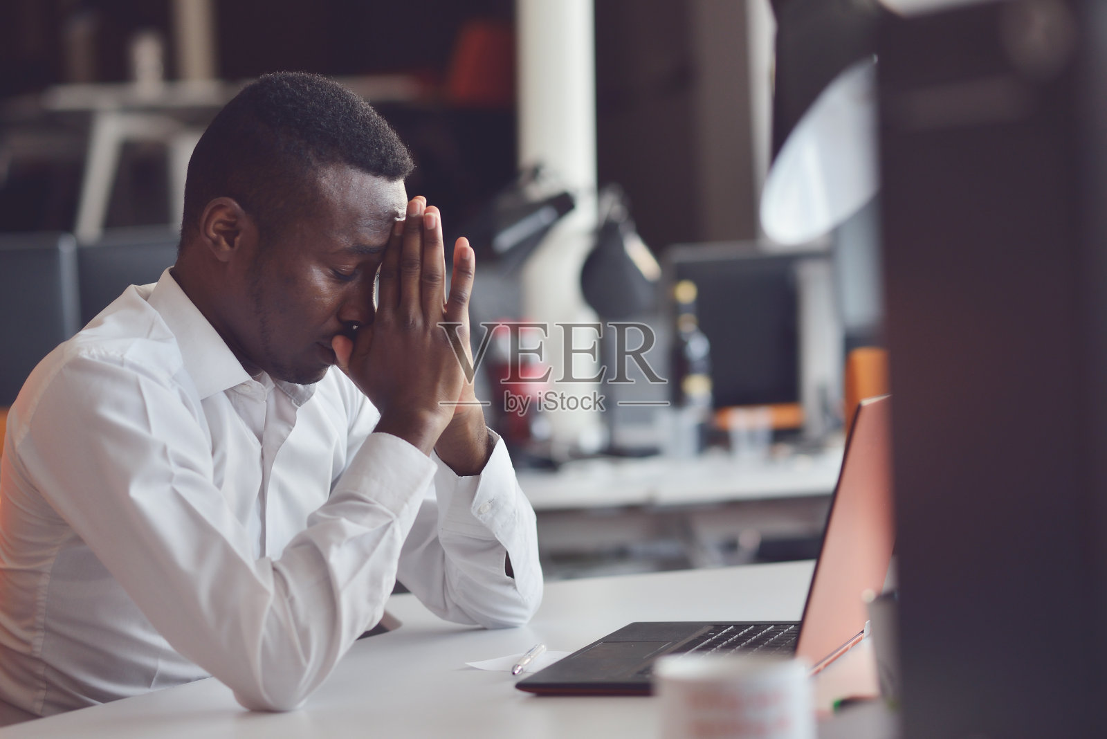 疲惫的非洲人在一个辛苦的工作日结束后坐在办公室里，用笔记本电脑工作，试图集中精力照片摄影图片