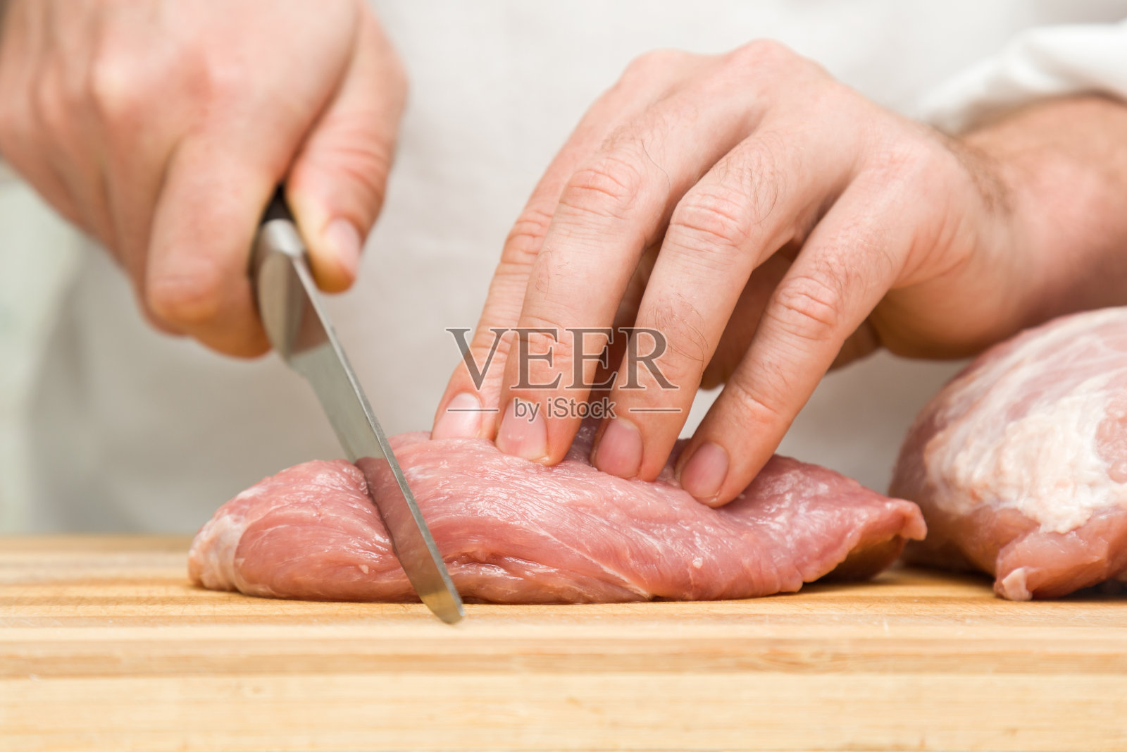 厨师的手拿着刀在厨房的木板上切着一块肉。准备做饭。食品的概念。照片摄影图片