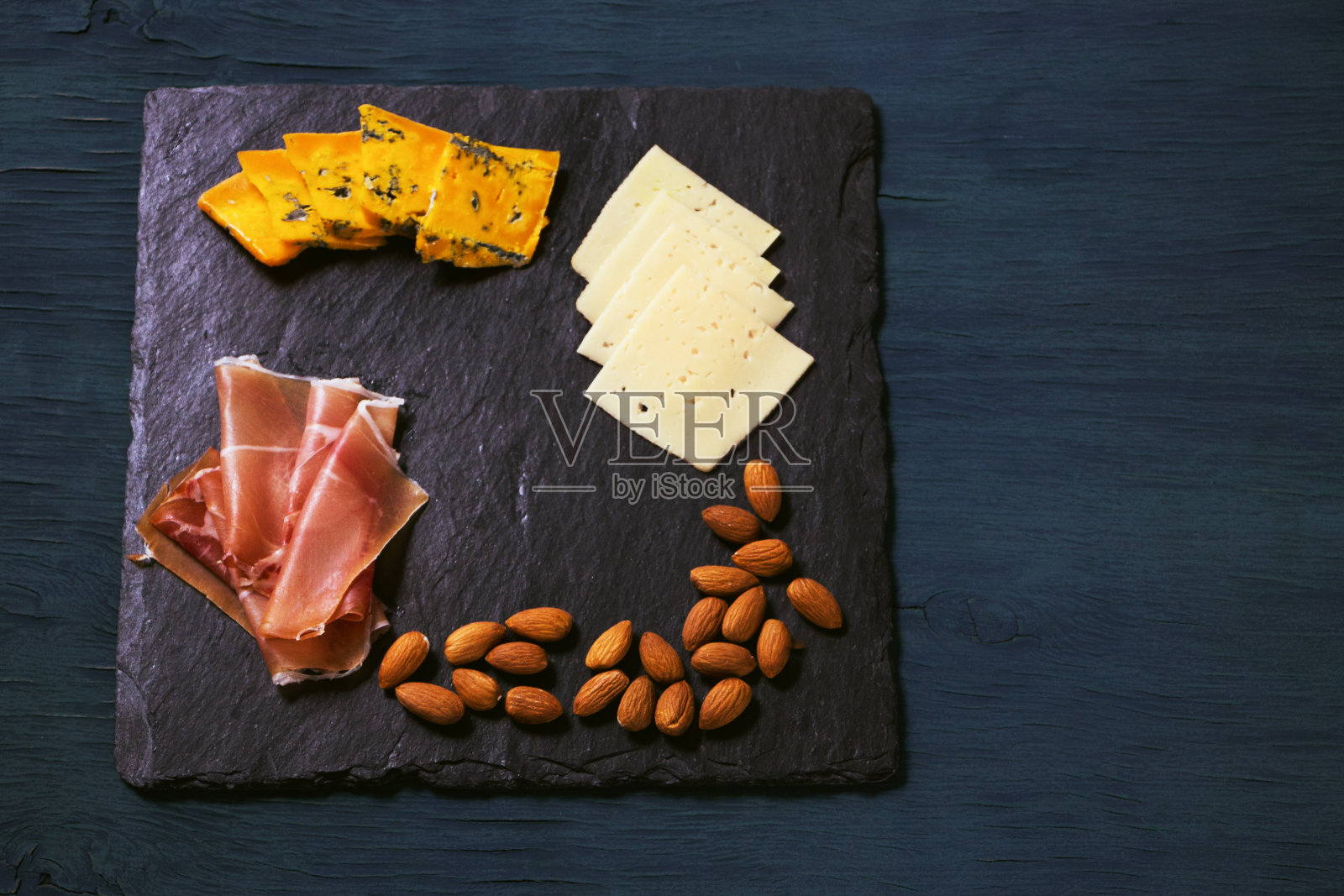 在深蓝色的背景下，石板托盘上放着零食和葡萄酒。奶酪、坚果、火腿。作者处理,copy-space照片摄影图片