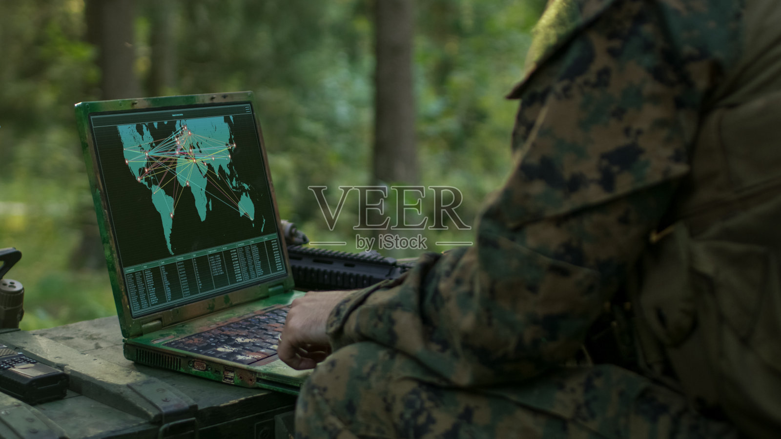 军事行动中，士兵使用军用级笔记本电脑使用军用工业复杂硬件完成国际任务。背景是森林里的迷彩帐篷。照片摄影图片