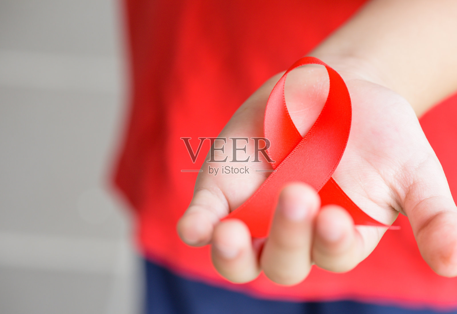 孩子手握红色的艾滋病宣传丝带。艾滋病宣传活动。照片摄影图片